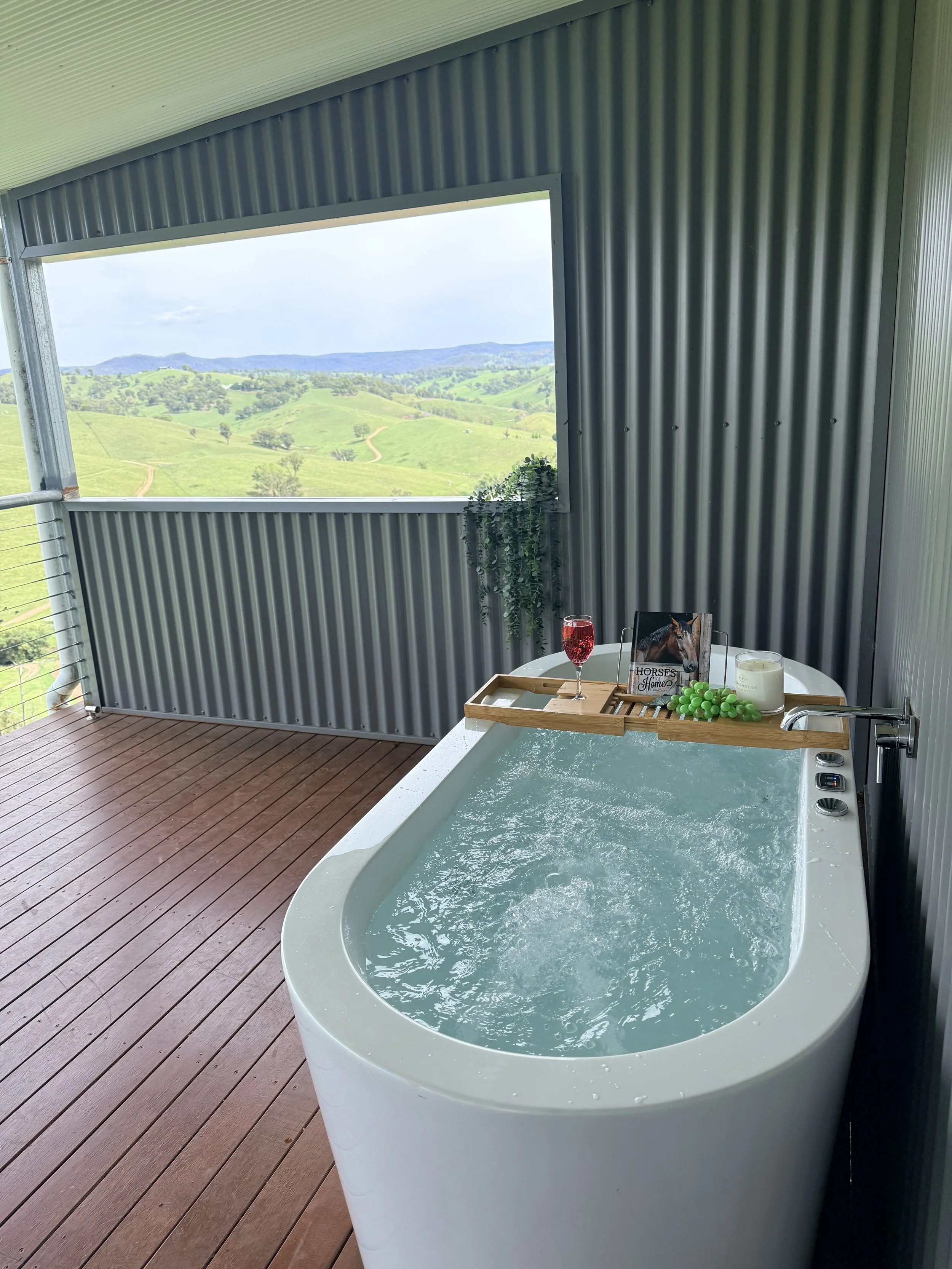 A small outdoor hot tub on a covered deck with a view of green rolling hills.