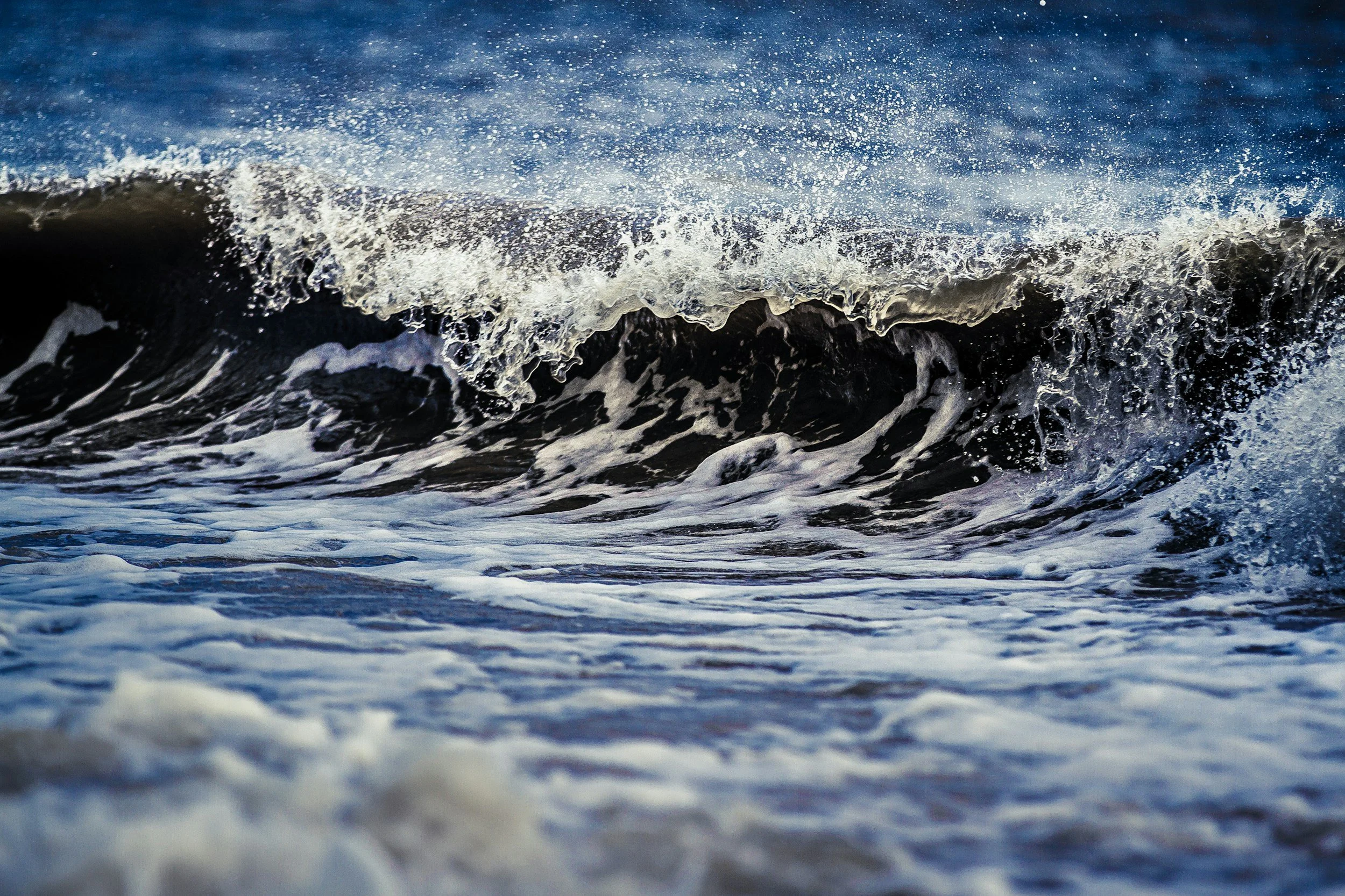 Waves crashing in the ocean with spray and foam, close-up view of water movement.