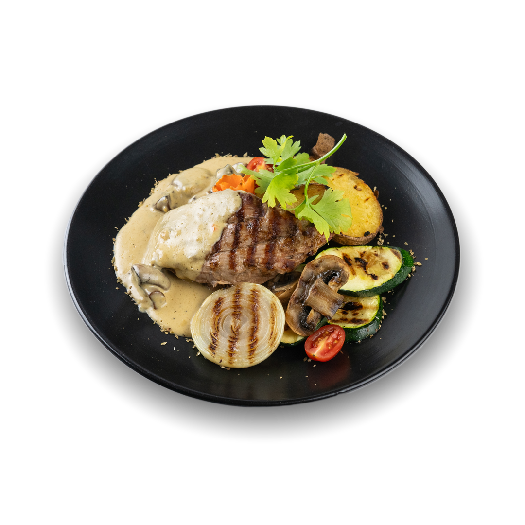 Ein Teller mit gegrilltem Steak, Zucchini, Champignons, Tomaten, Auberginen, Kartoffeln, Zwiebel und einer weißen Soße, garniert mit frischer Petersilie auf einer schwarzen Platte.