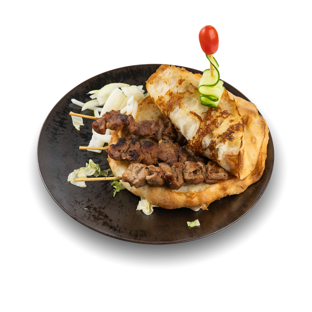 Hauptgericht mit süßem Pfannkuchen, gegrilltem Fleisch am Spieß, frittiertem Teig und Gemüse auf einem schwarzen Teller