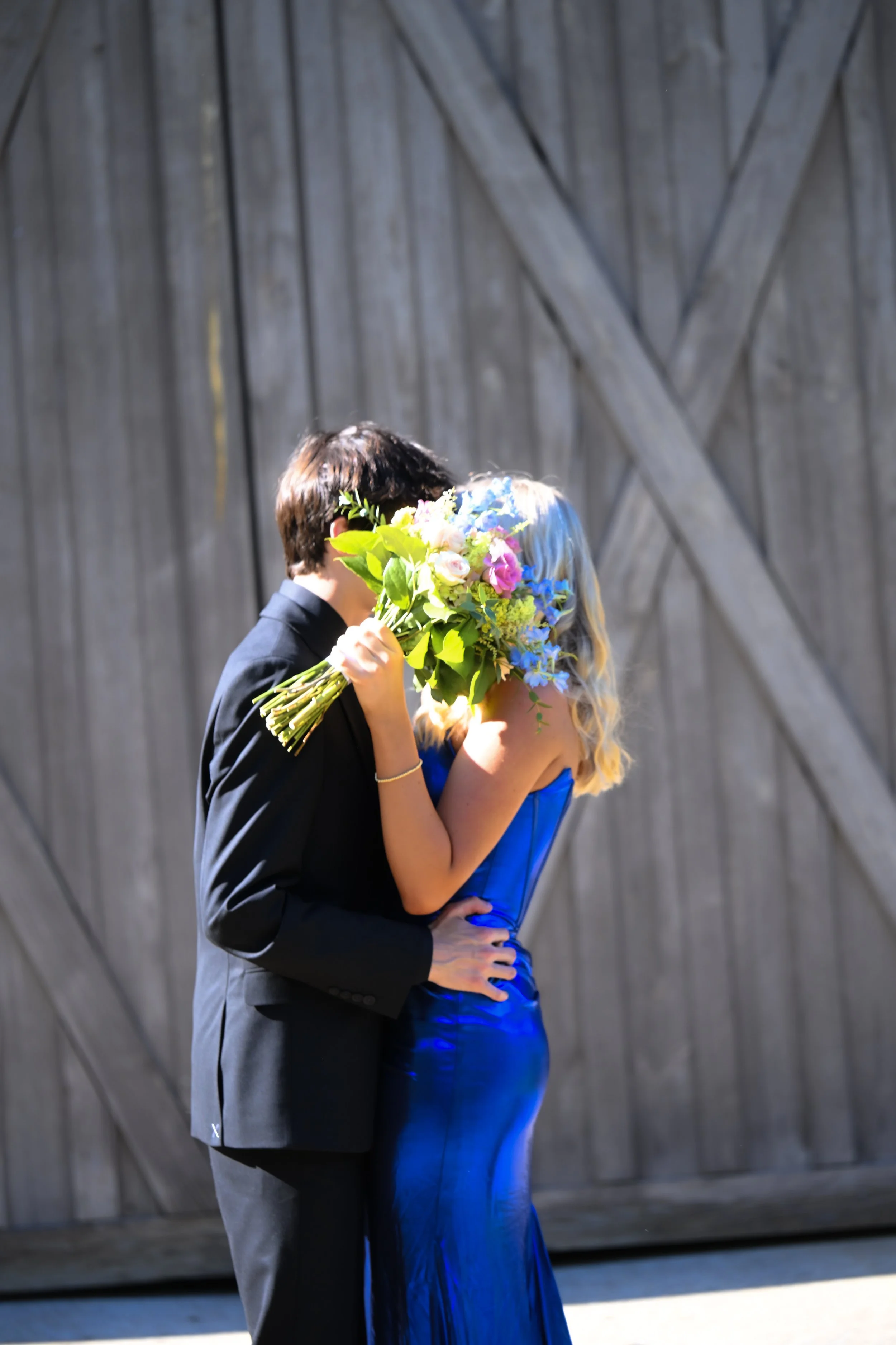 A couple sharing a kiss at an outdoor wedding ceremony, with the bride holding a bouquet of colorful flowers.