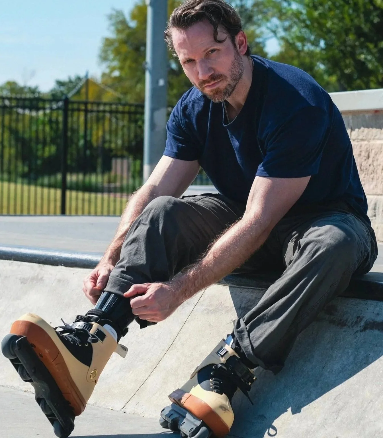 A man sitting on the edge of a skatepark, adjusting his rollerblades.