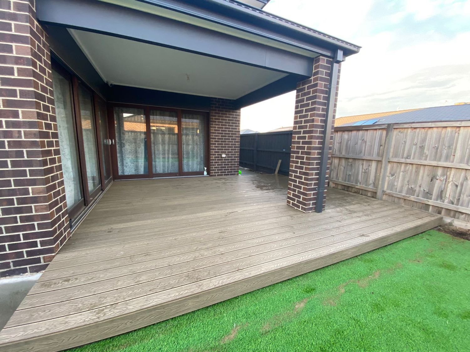 Backyard patio with a wooden deck, brick house exterior, sliding glass doors, and a wooden fence.