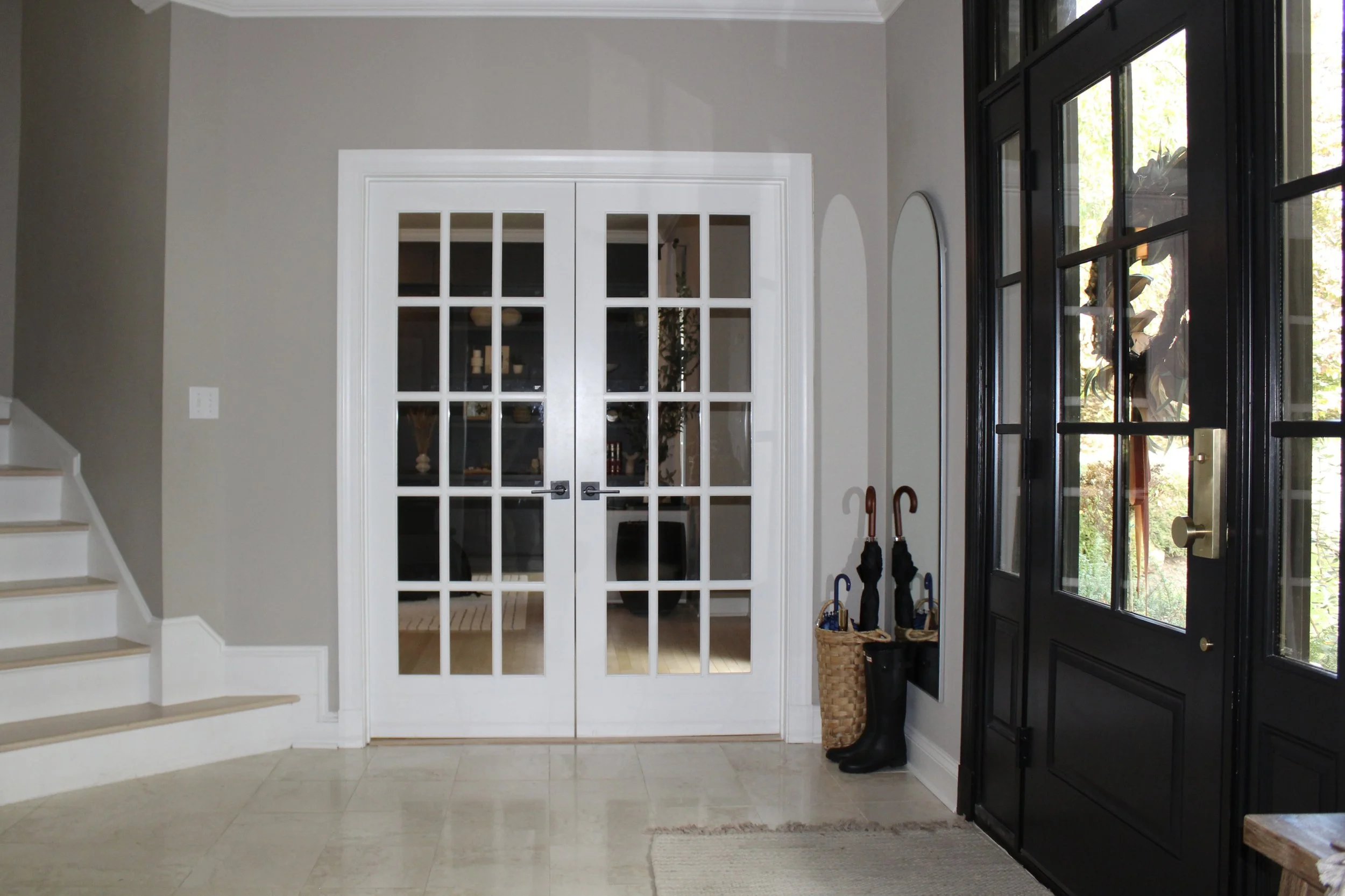 Entryway with black front door, white double glass doors, staircase to the left, and umbrellas and basket beside the glass doors.