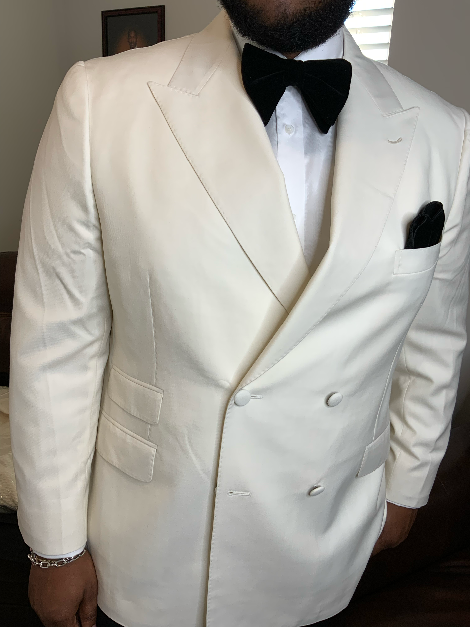 Man dressed in a white tuxedo with black bow tie, standing indoors.