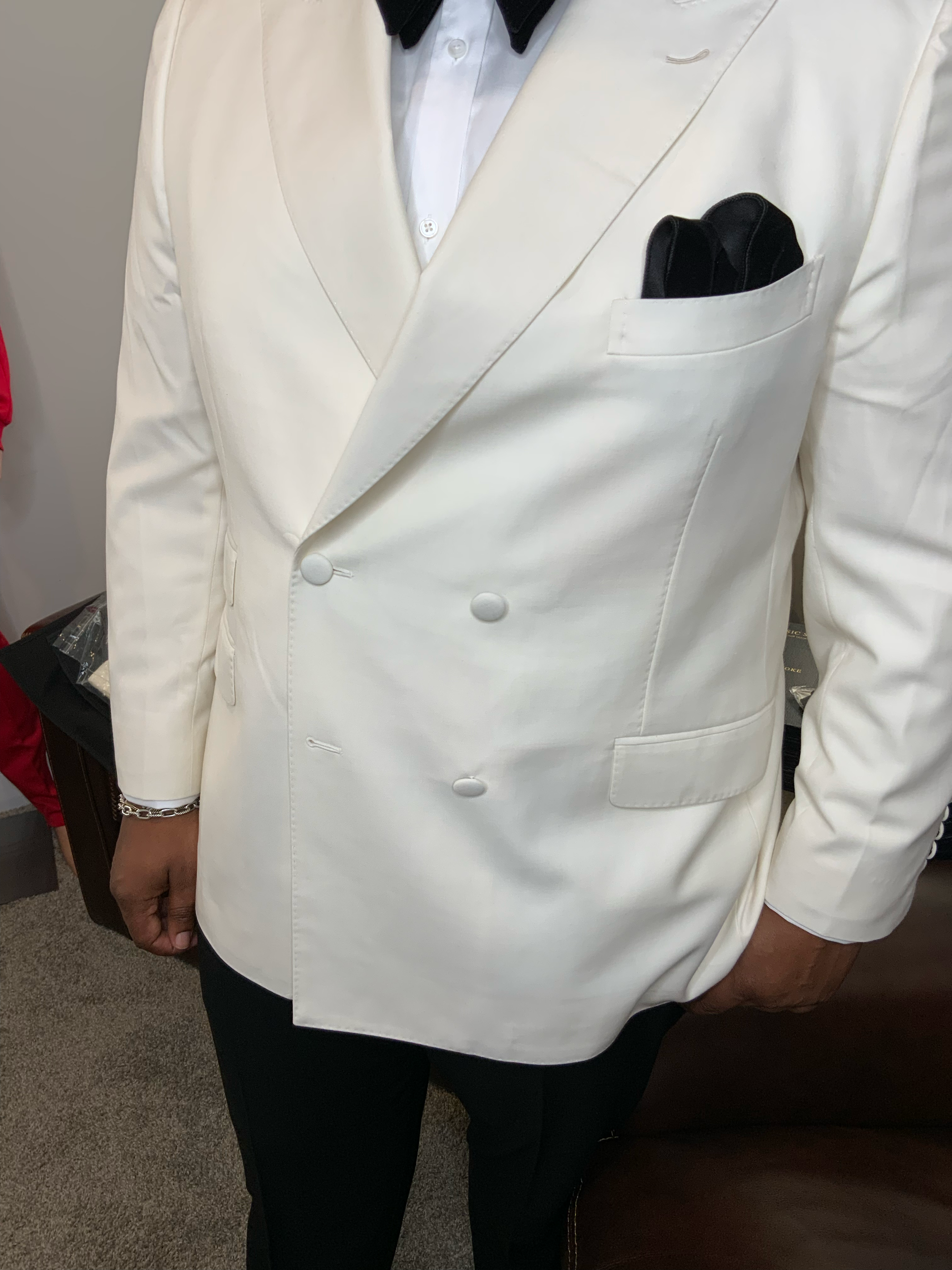 A person wearing a white blazer, with a black shirt underneath, and black pants, standing indoors.