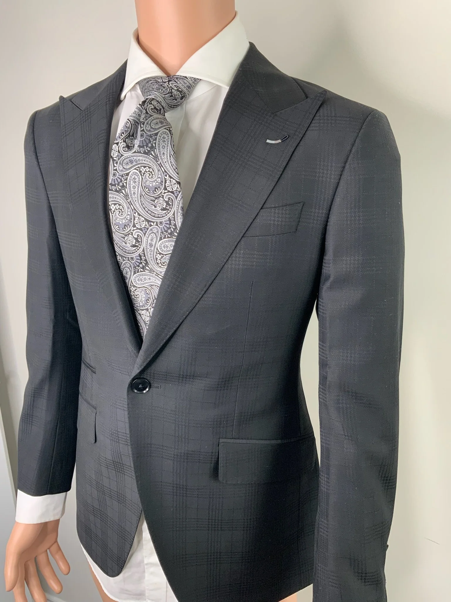 Mannequin dressed in a dark gray checked suit, white dress shirt, patterned tie, and white undershirt, against a plain background.