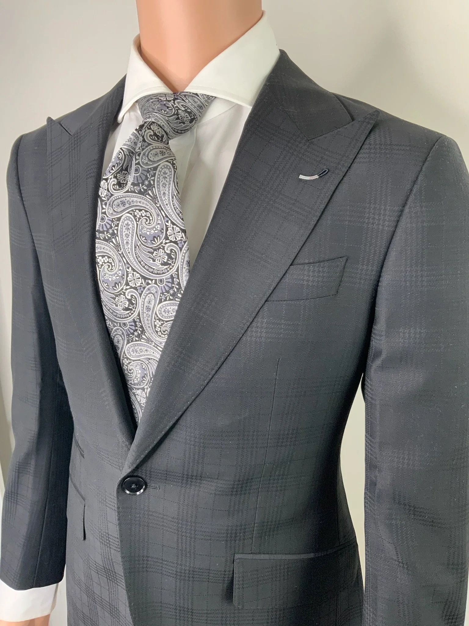 Close-up of a mannequin dressed in a dark gray plaid suit, white dress shirt, and a patterned tie.