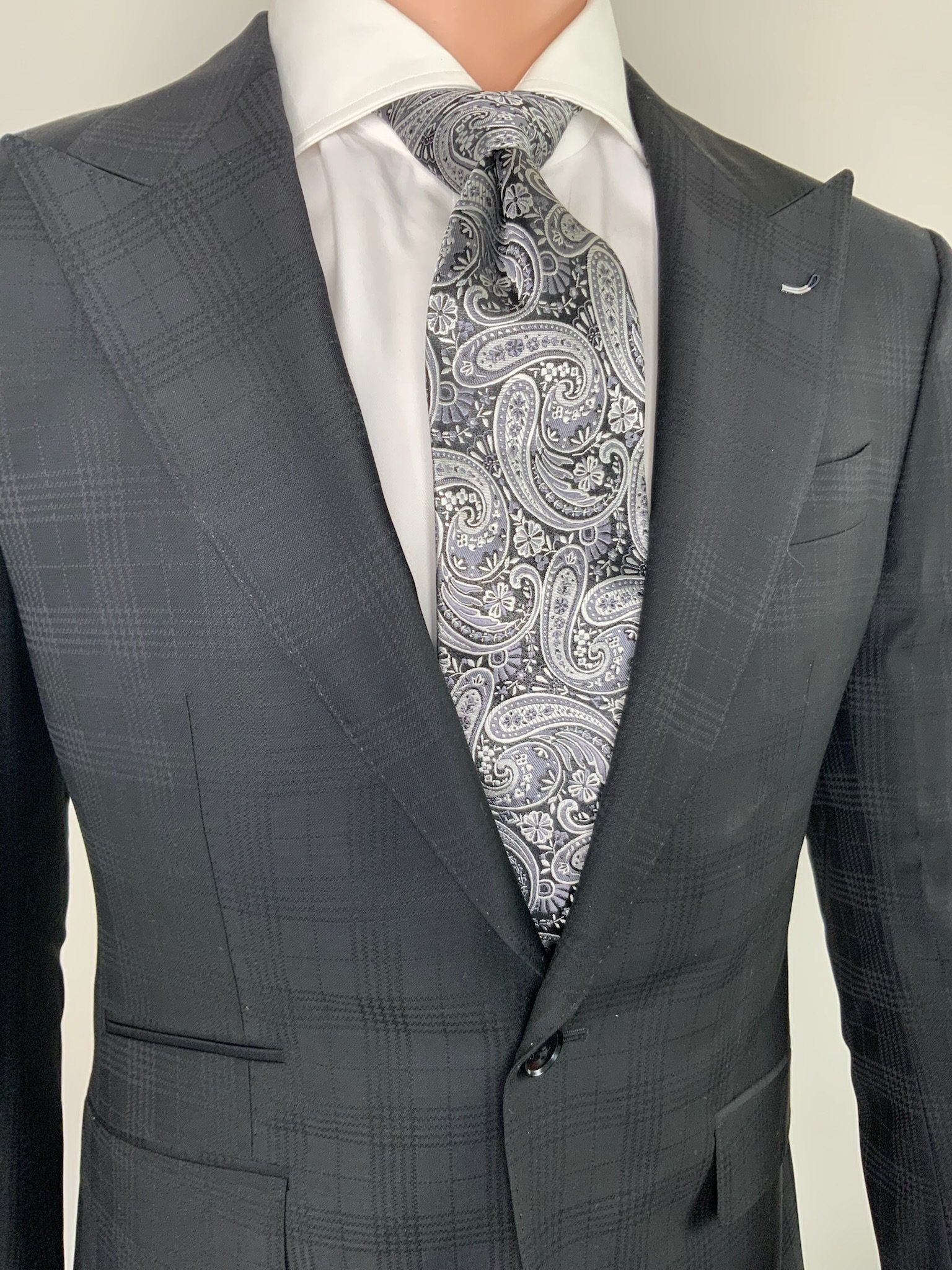 Close-up of a man wearing a dark plaid suit, white dress shirt, and a paisley patterned tie.