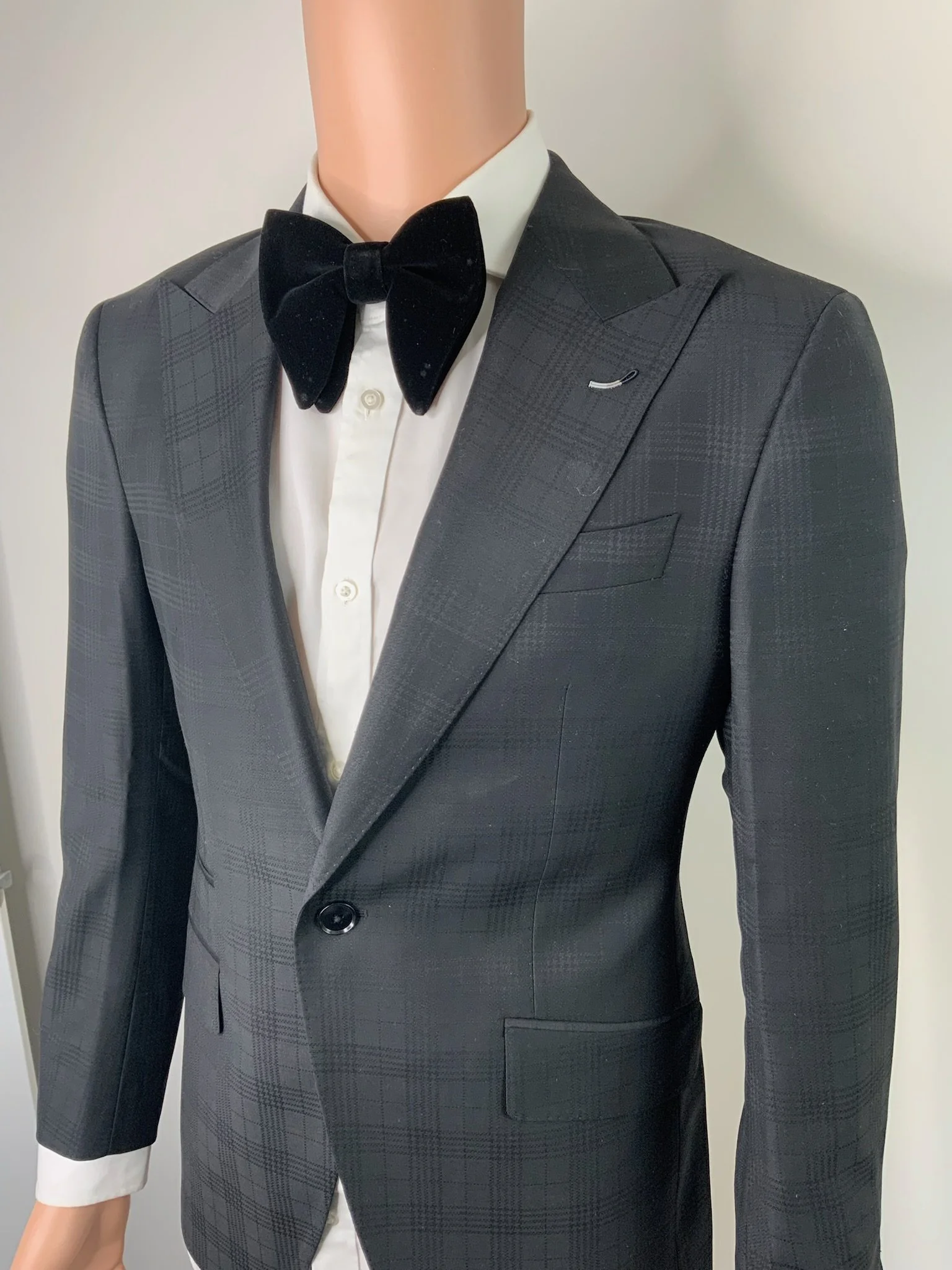 Mannequin dressed in a black tuxedo with a white shirt and black bow tie, against a plain background.
