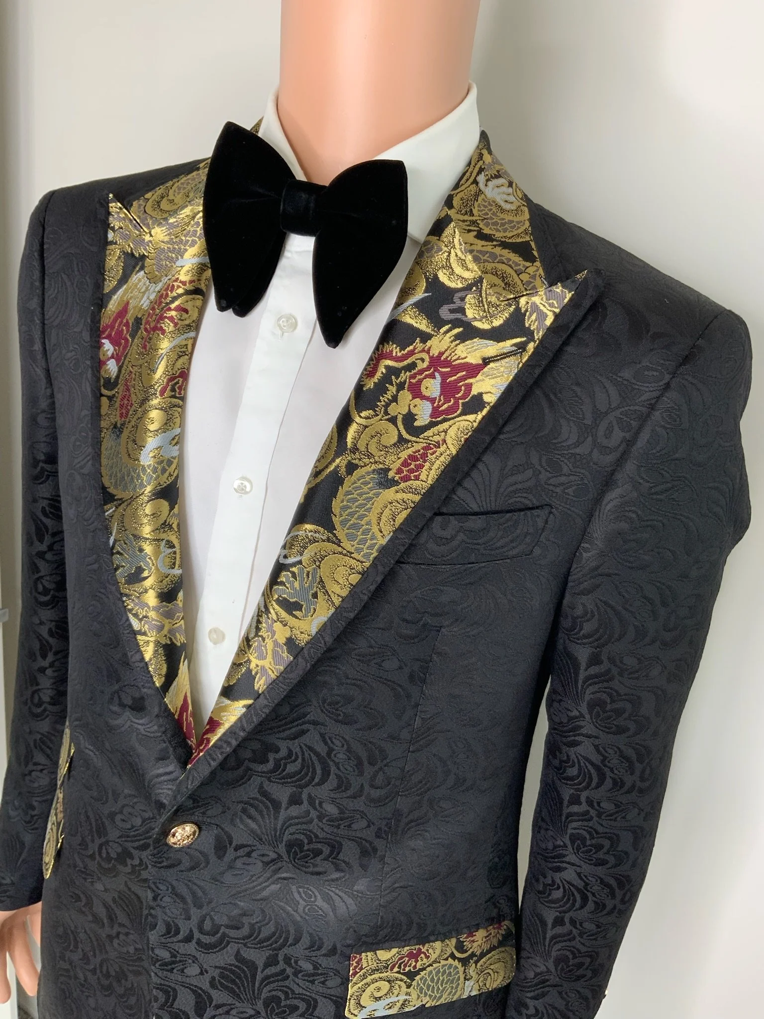 Close-up of a tuxedo with black and gold embroidered jacket, white shirt, and black bow tie on a mannequin.