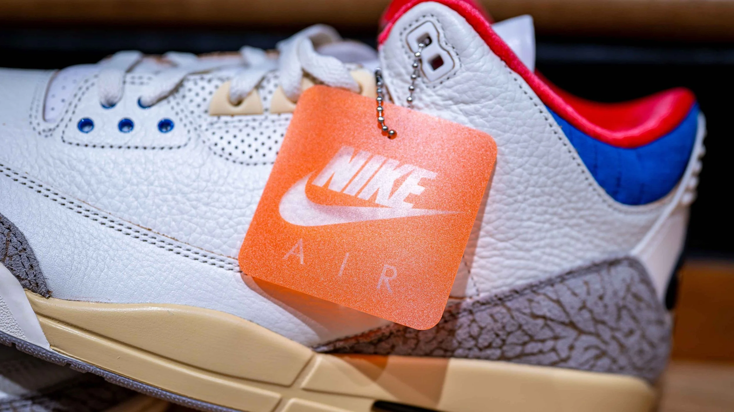 Close-up of a Nike Air sneaker with a bright orange Nike Air tag attached to the laces.