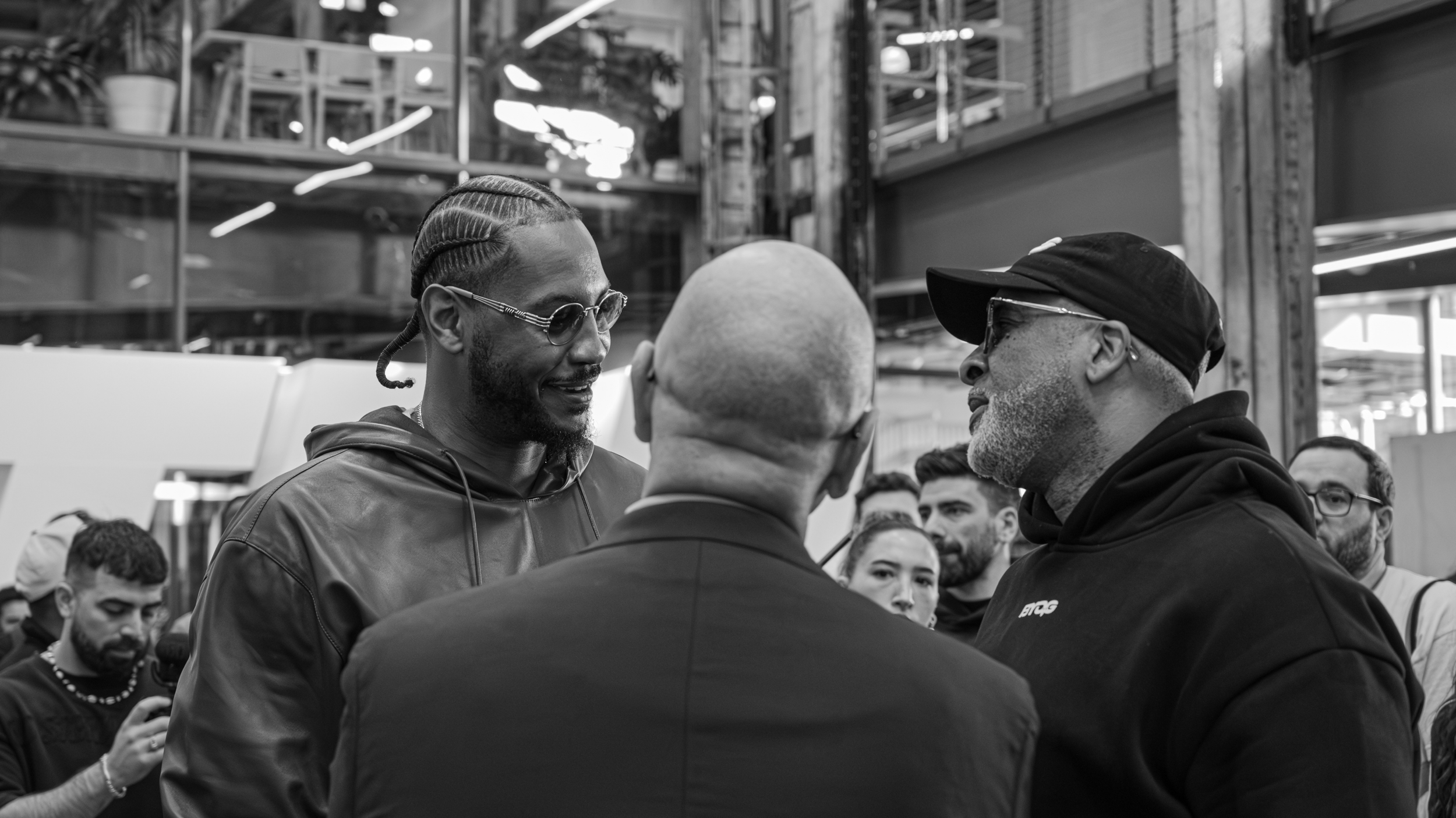 Three men in a discussion at a public event, with a crowd of people in the background.