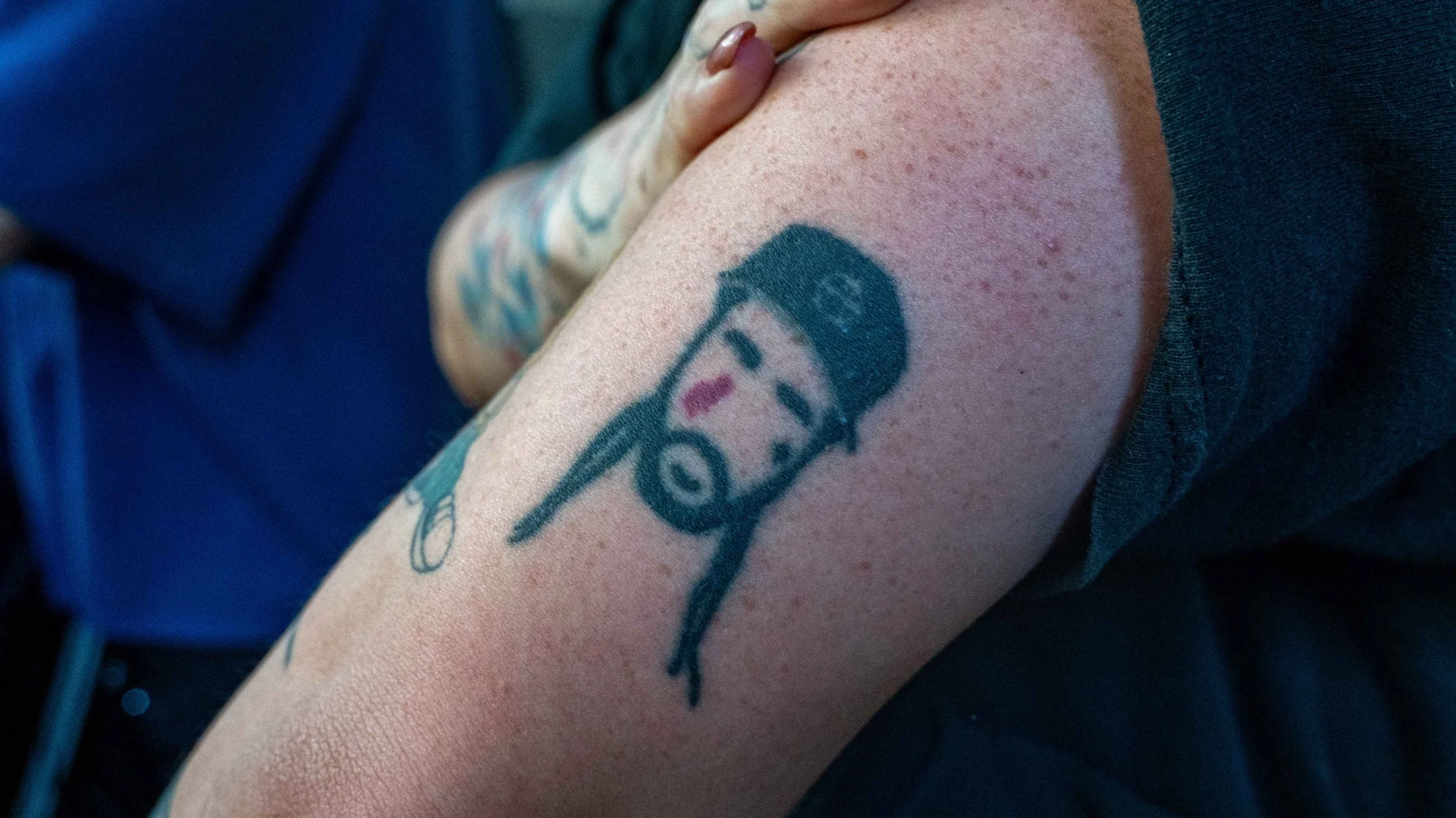 Tattoo of a character with a baseball cap and a chain on a person's upper arm.