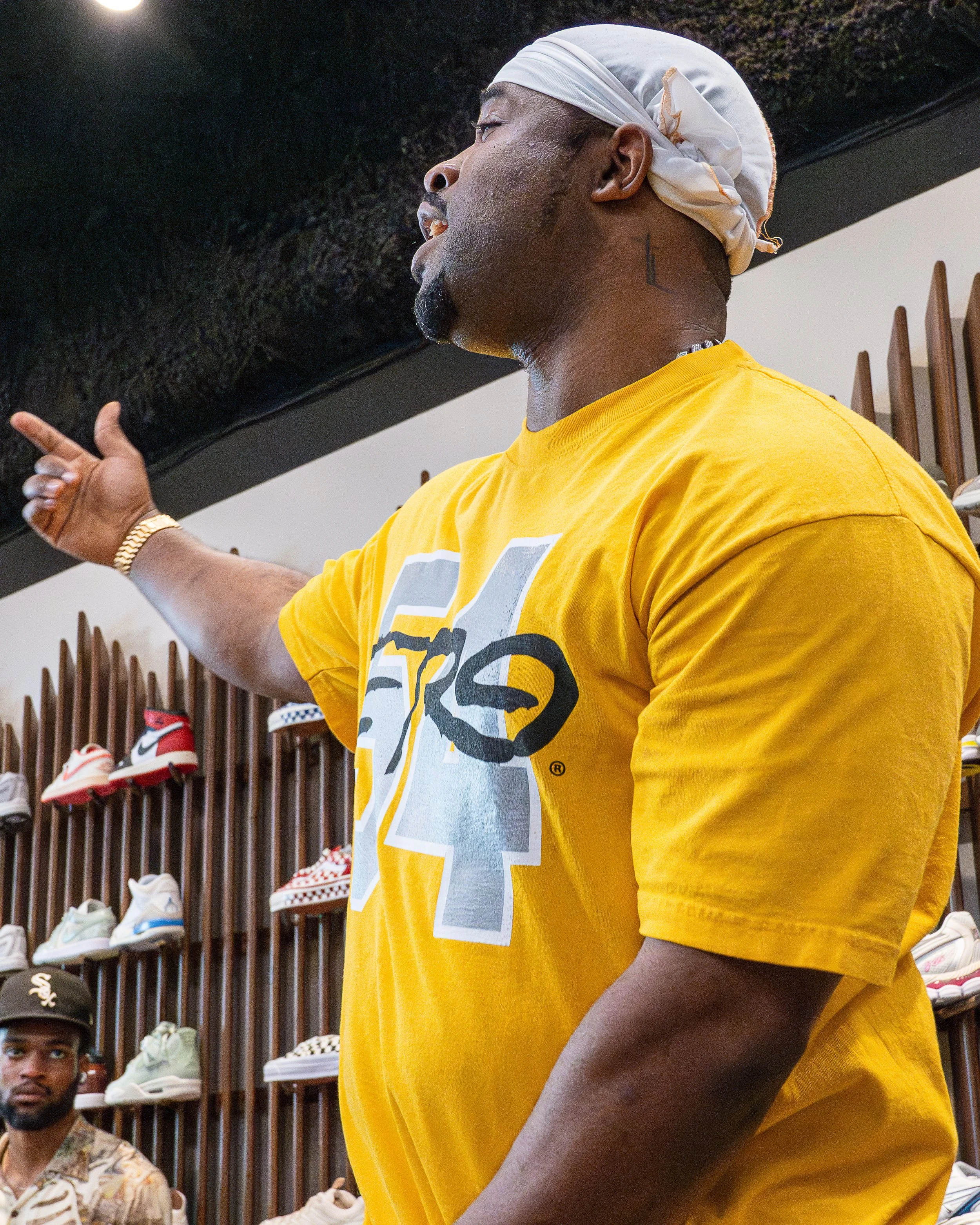 Artist dancing passionately in a sneaker store with shoes displayed behind him, photographed by HigherLXNG.
