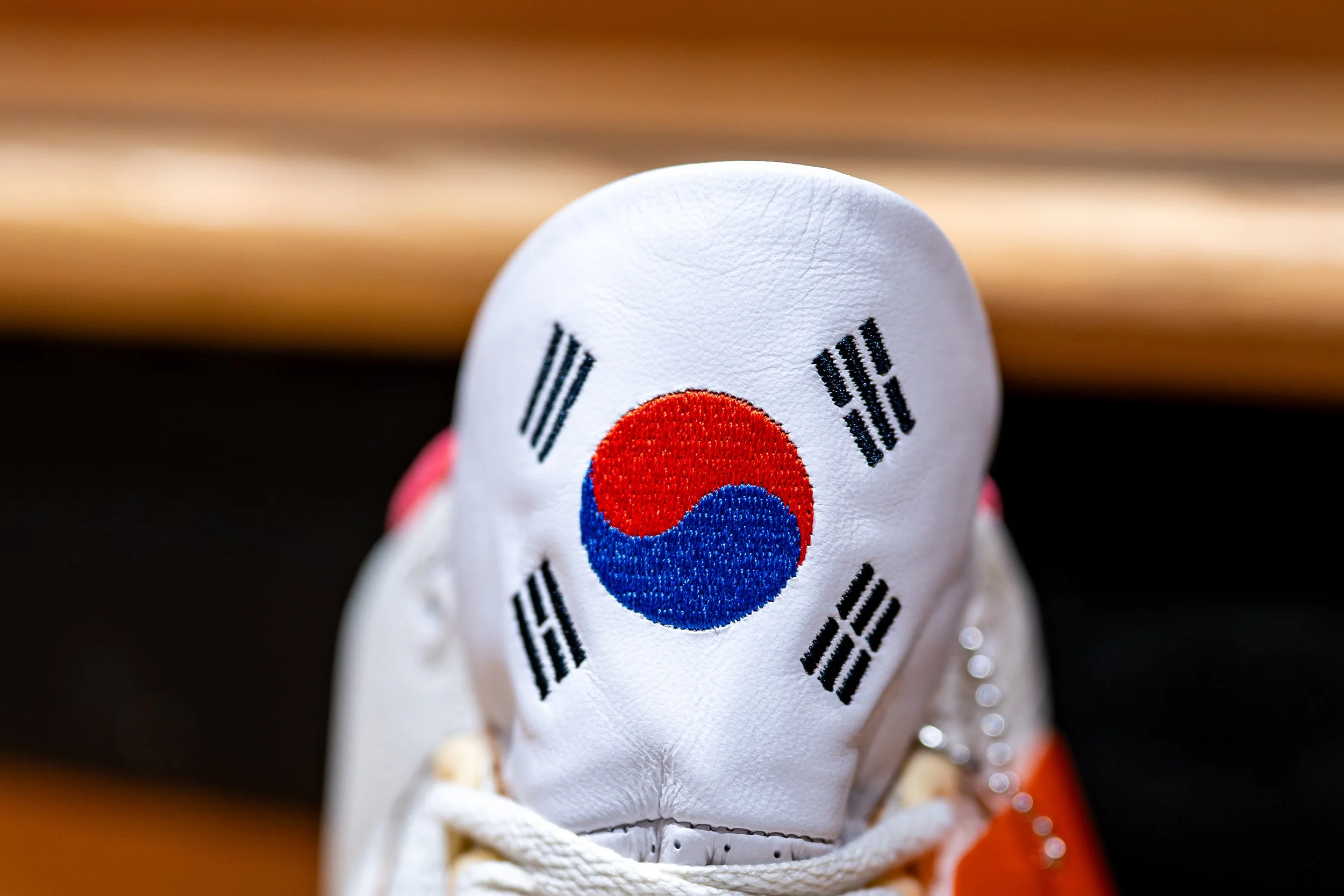 Close-up of a white sneaker with the South Korean flag embroidered on the toe area, featuring a red and blue yin-yang symbol and black trigrams.