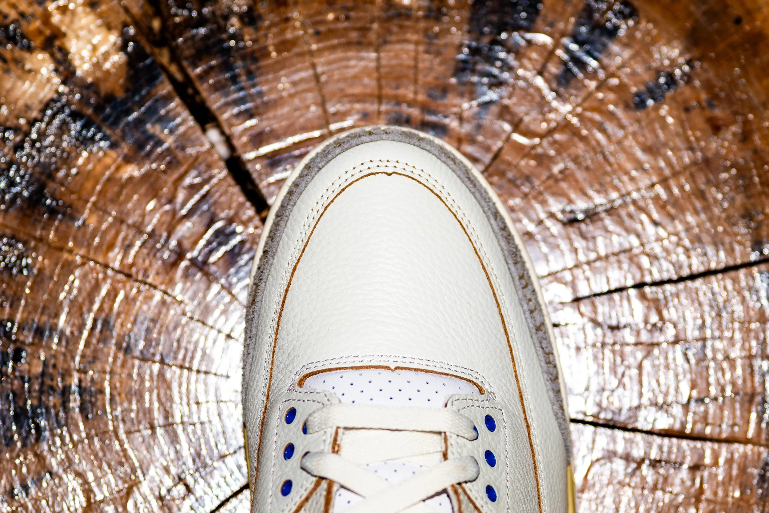 Close-up of a white sneaker on a wooden surface with visible grain and cracks.