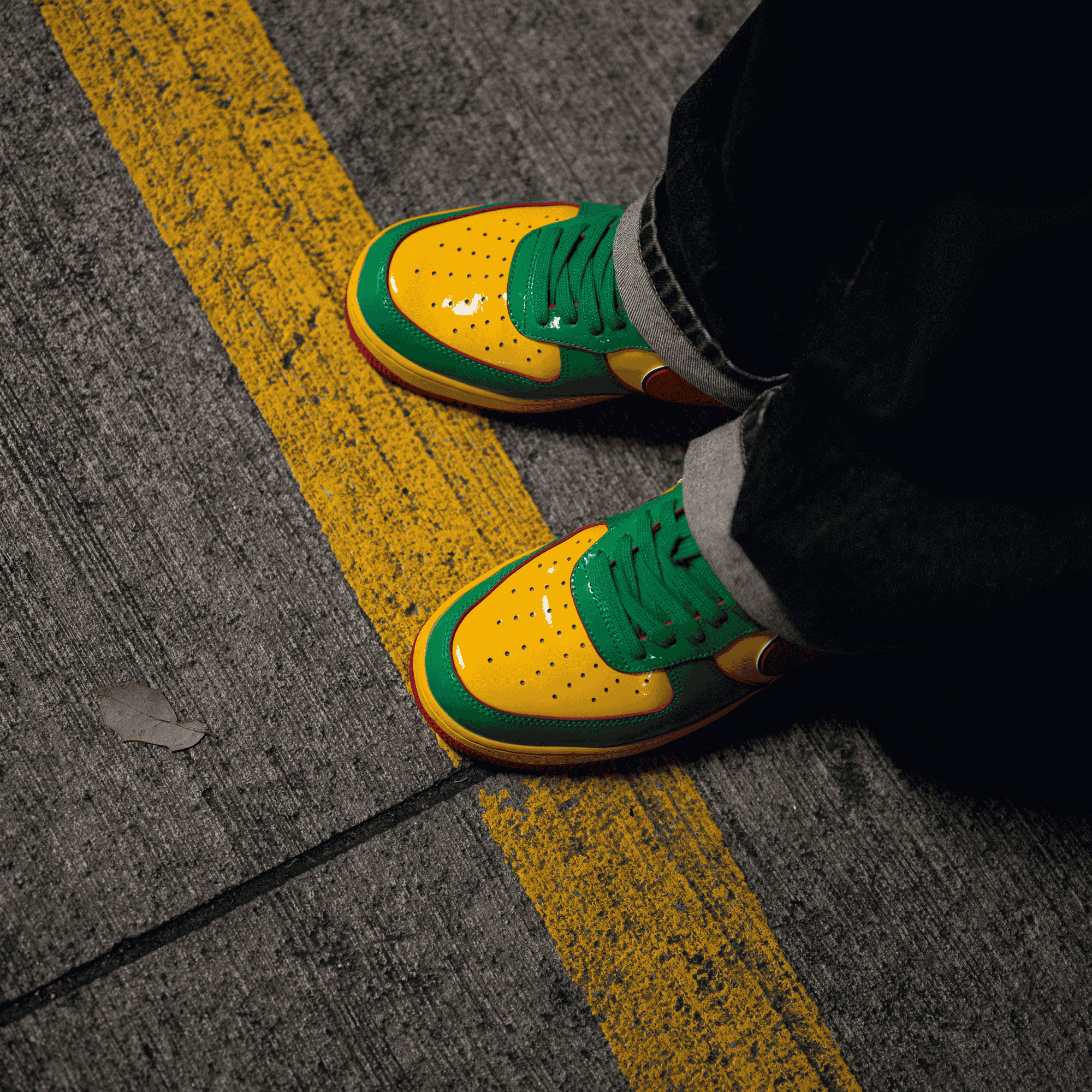 Person wearing yellow, green, and red sneakers standing on a street with a yellow line.
