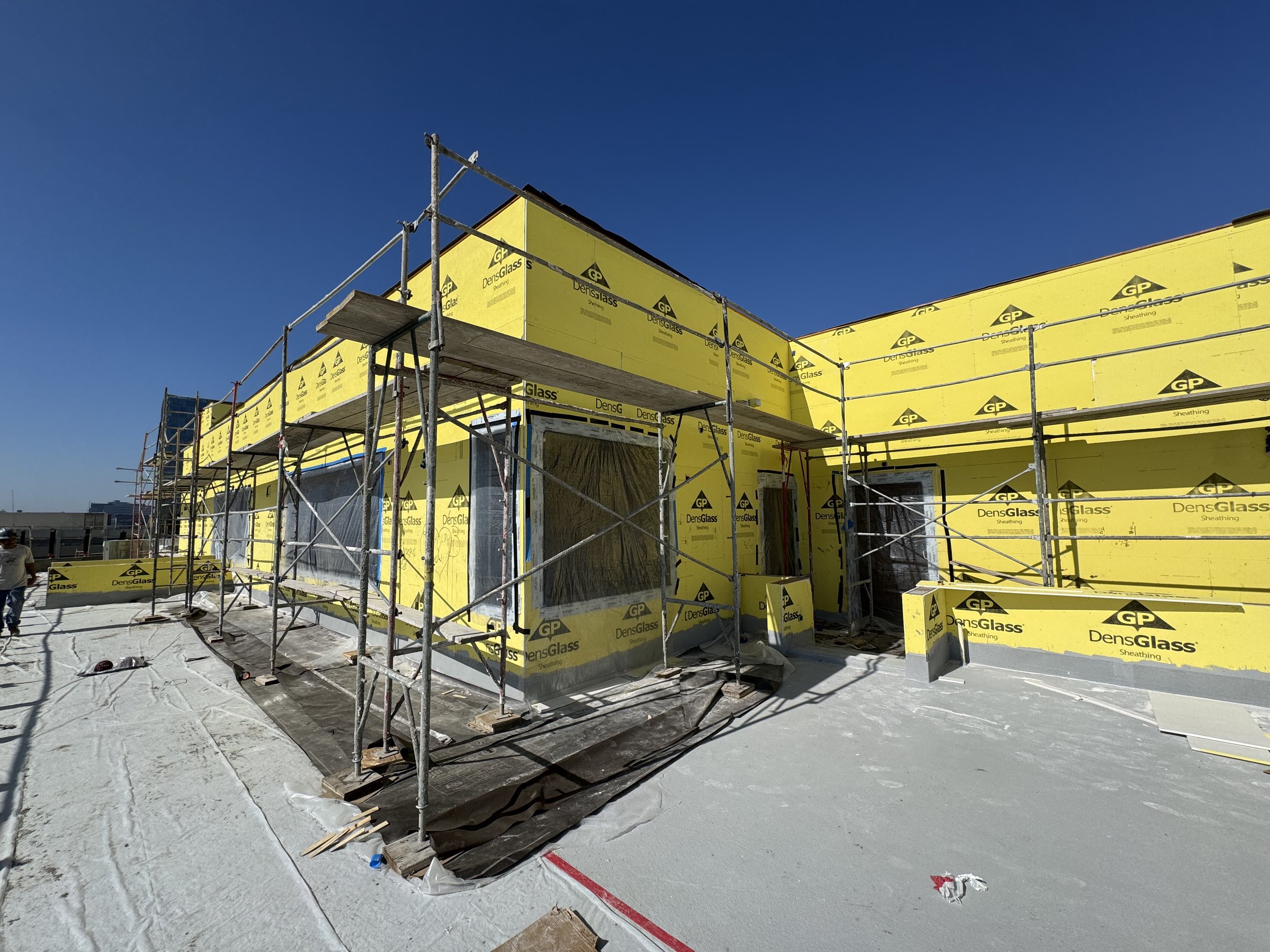 Construction site on a building rooftop with yellow wall insulation and scaffolding, under a clear blue sky.