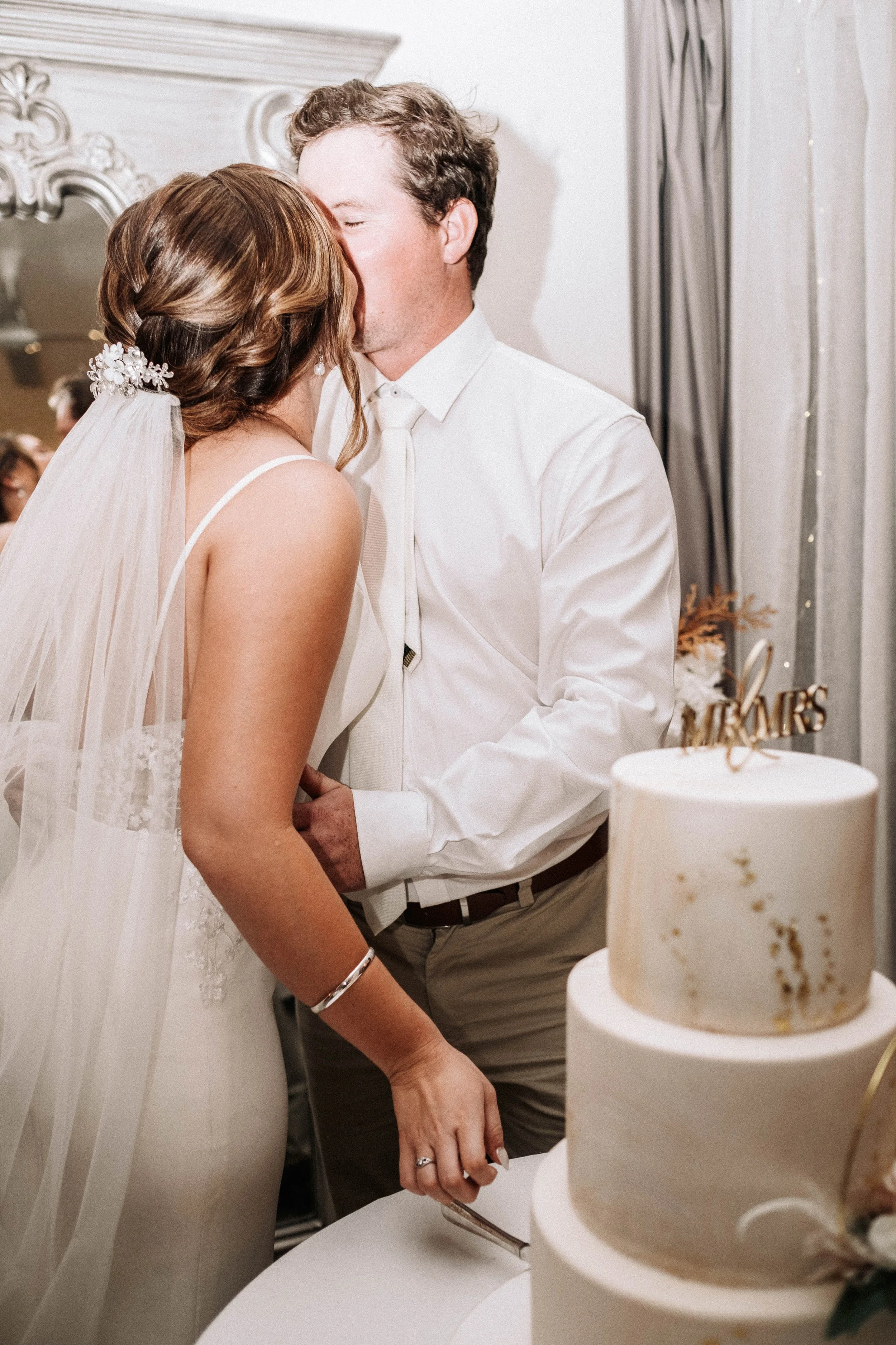 Bride and groom kiss during cake cutting at wedding reception in Yeppoon
