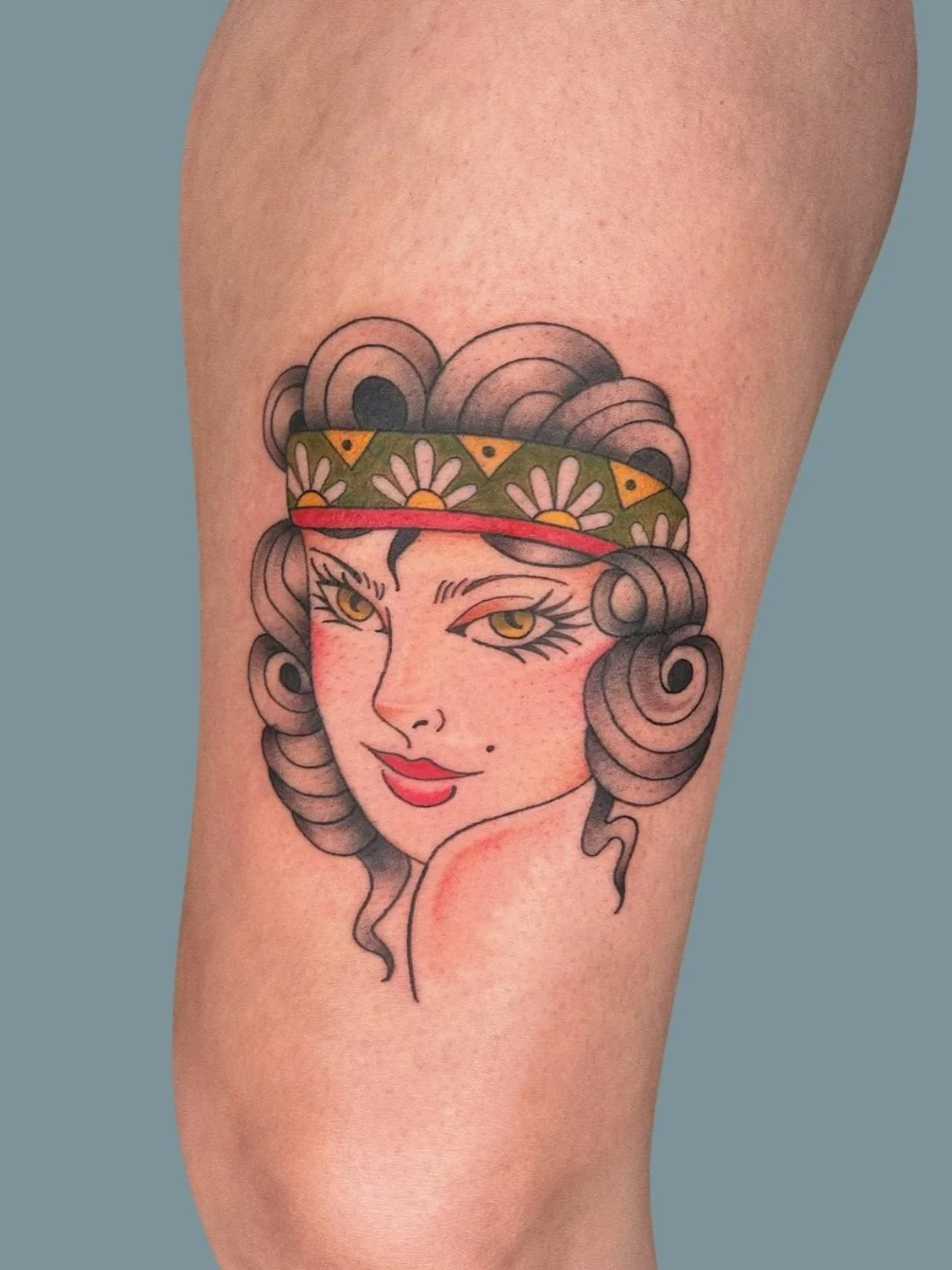 Tattoo of a woman with curly hair, wearing a green headscarf with yellow flowers, with a confident expression.