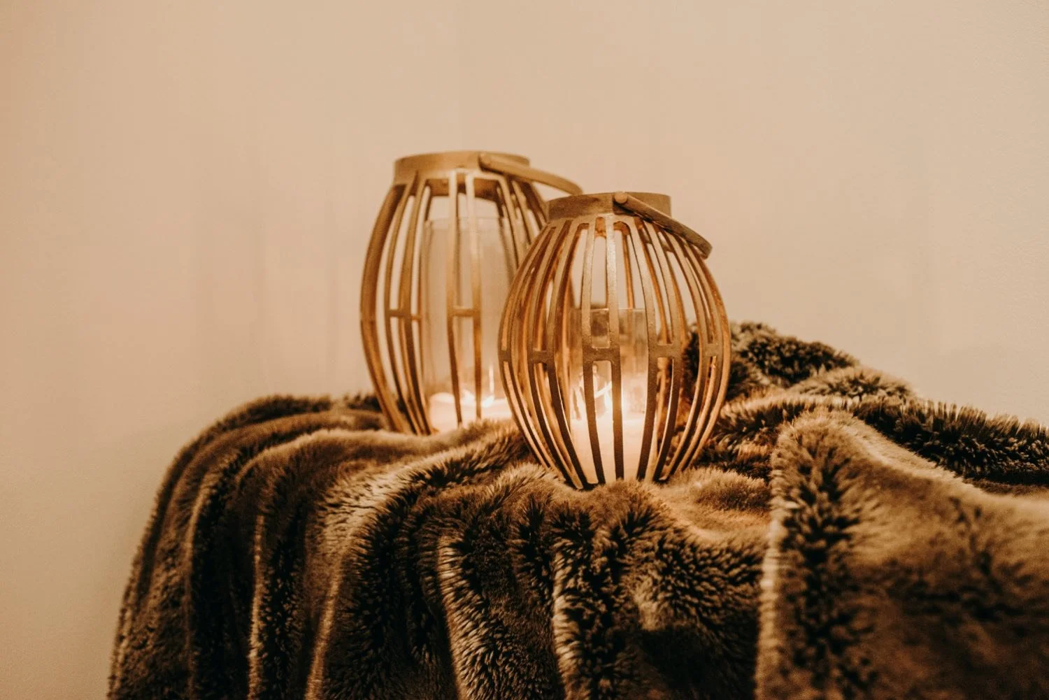 Two wooden lanterns with candle flames inside, placed on a soft, textured blanket.