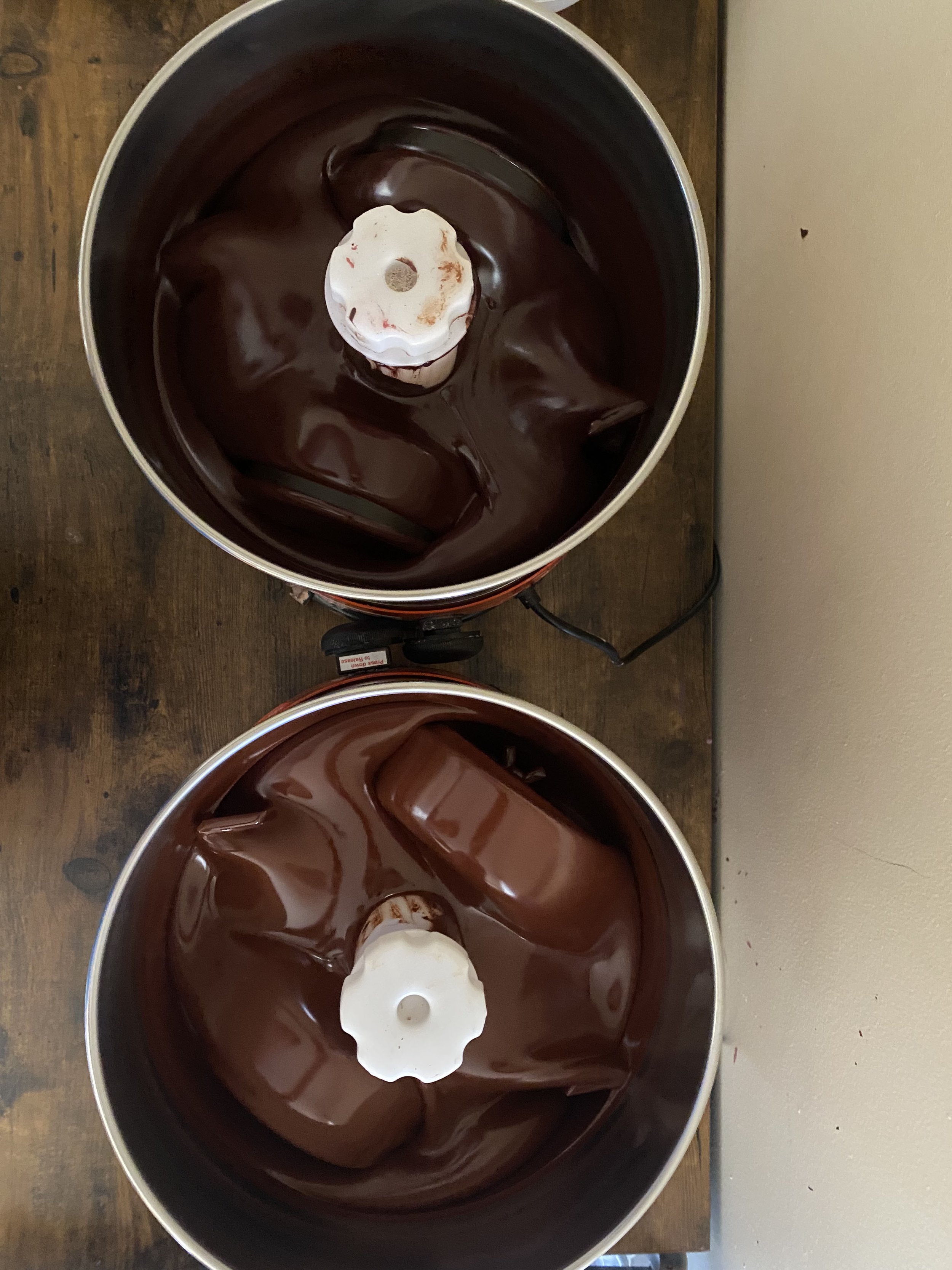 Two slow cookers filled with melted chocolate, placed on a wooden surface.