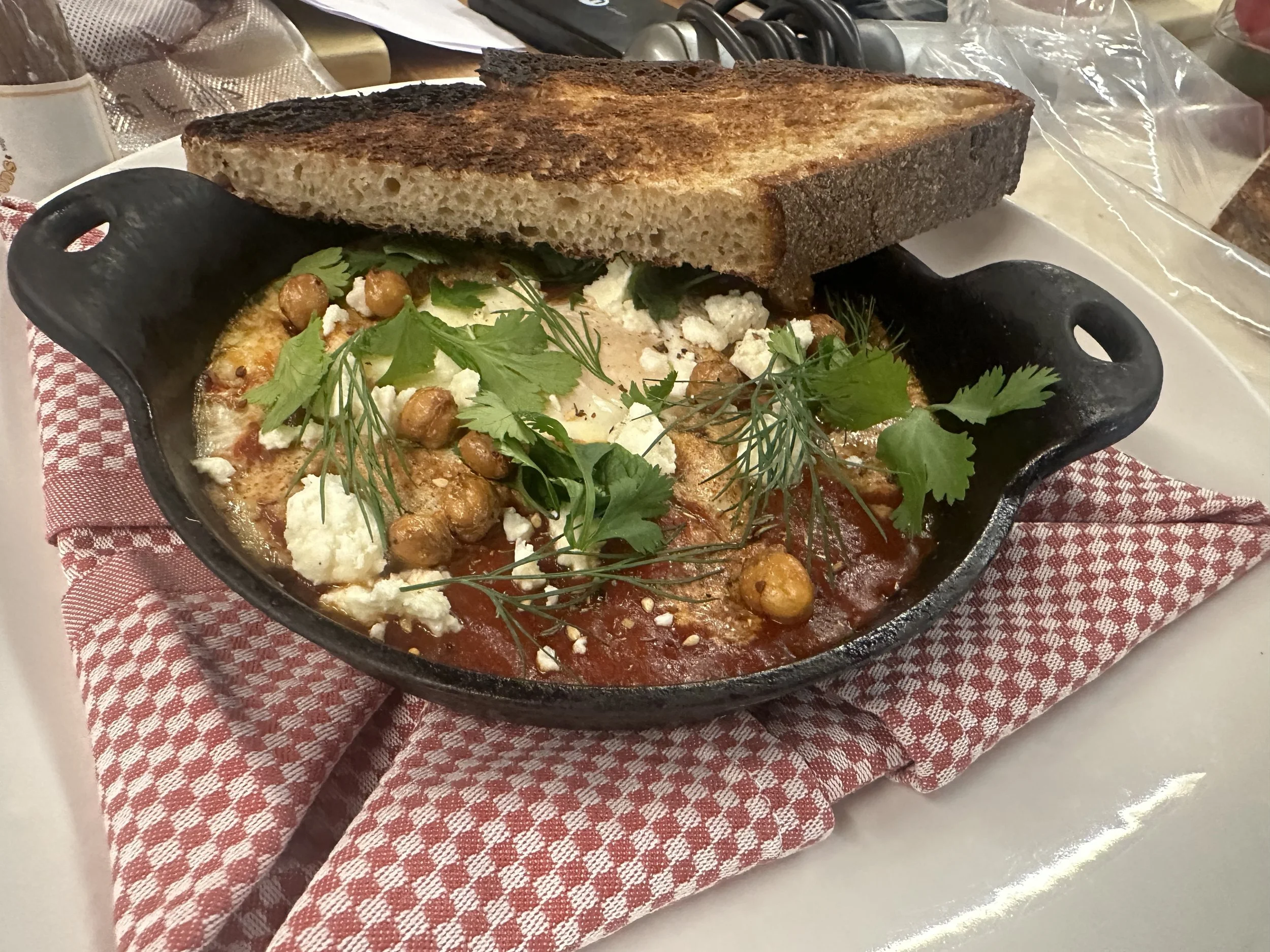 Chickpea shakshuka in a cast iron skillet topped with herbs and crumbled cheese, served with toasted bread on top.