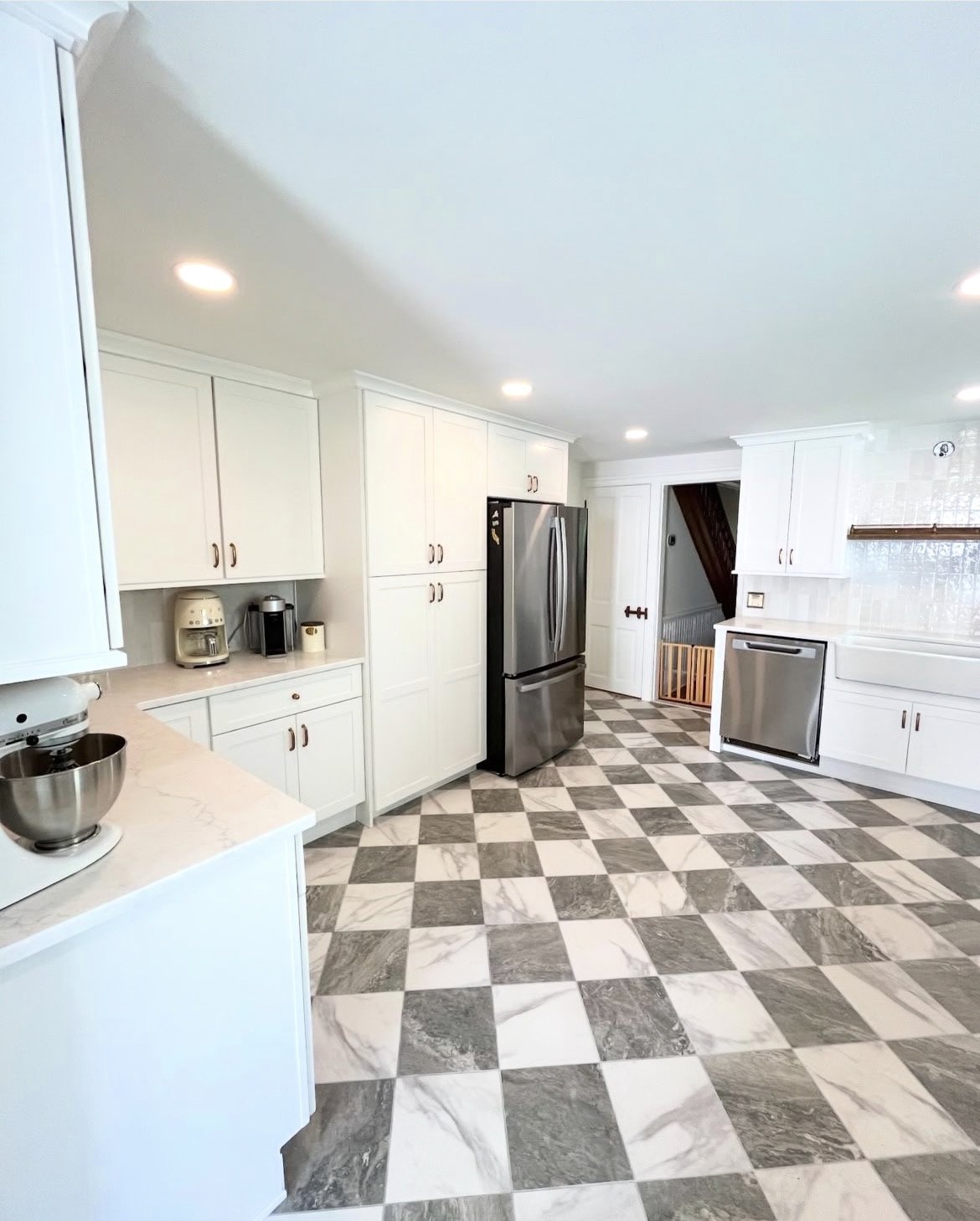 A modern kitchen with white cabinets, stainless steel refrigerator, and a black and white checkered marble floor.