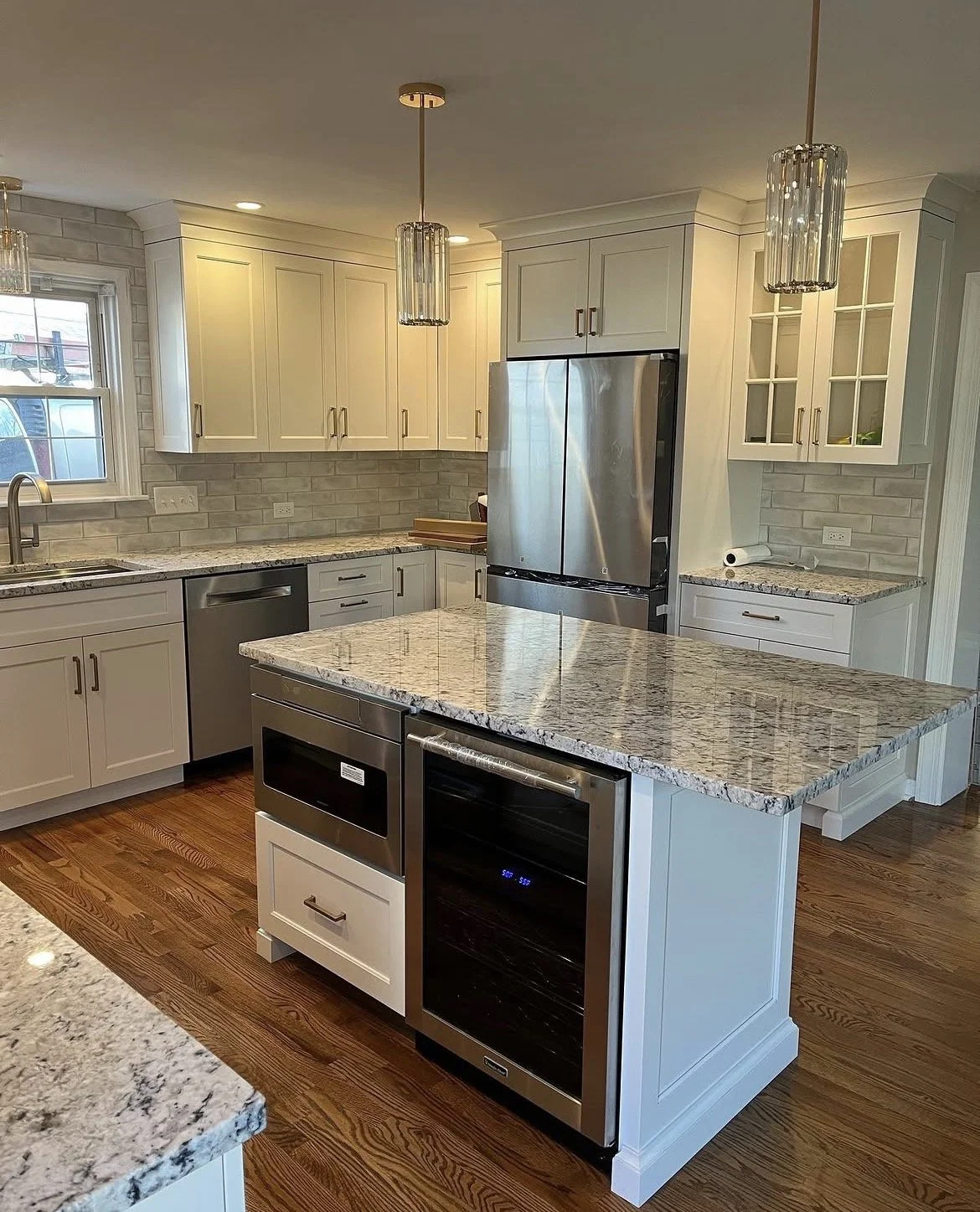 Modern kitchen with white cabinetry, granite countertops, and stainless steel appliances including a refrigerator, microwave, and dishwasher. MGD takes pride in your kitchen remodel.