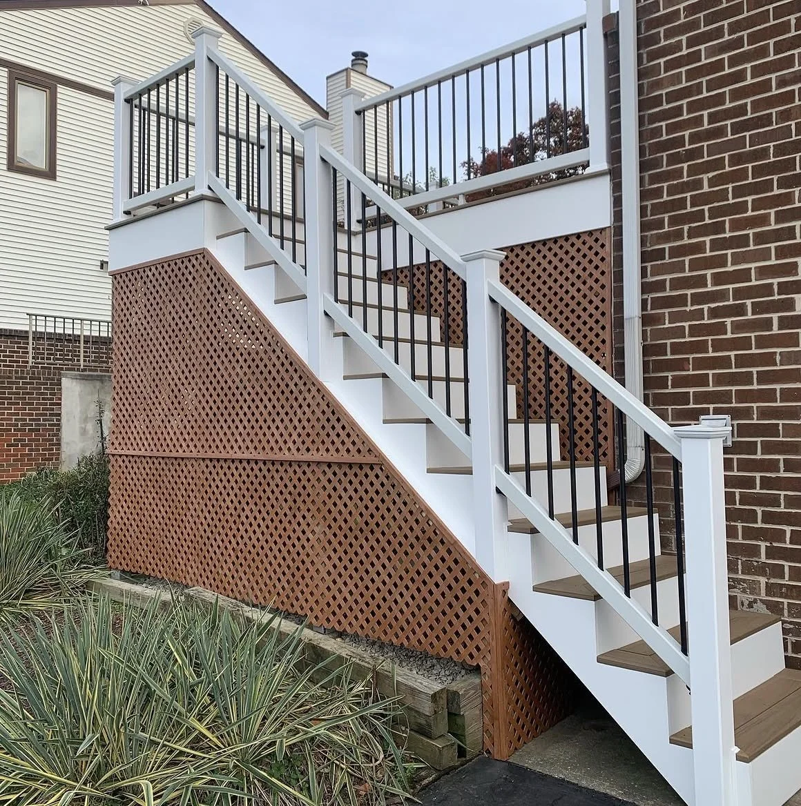 Outdoor staircase with white risers, brown treads, black railing, and lattice skirting. MGD Carpentry here to refresh your deck or patio today!