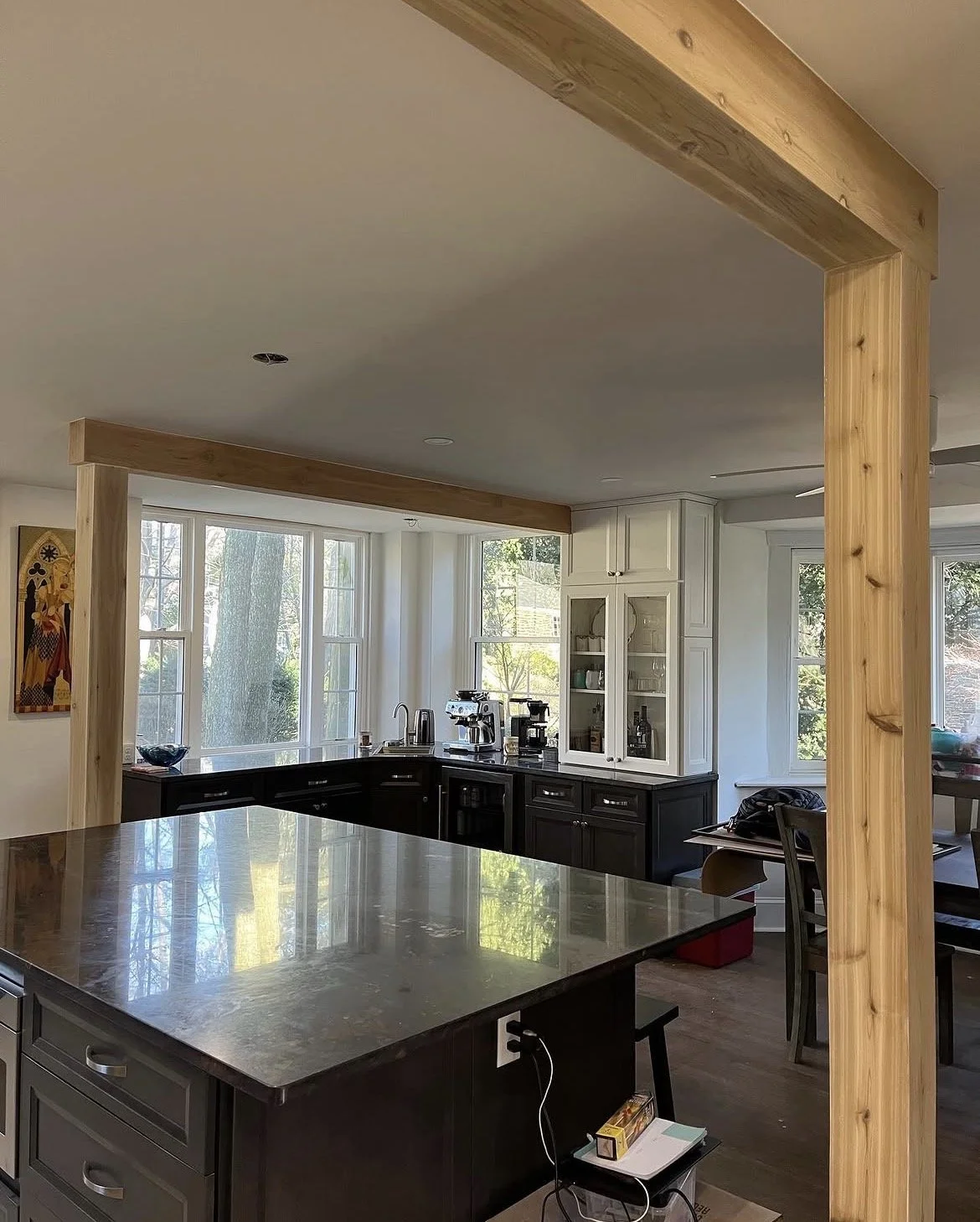 Modern kitchen with large window, black and white cabinetry, and a wooden supportive frame or partial wall.