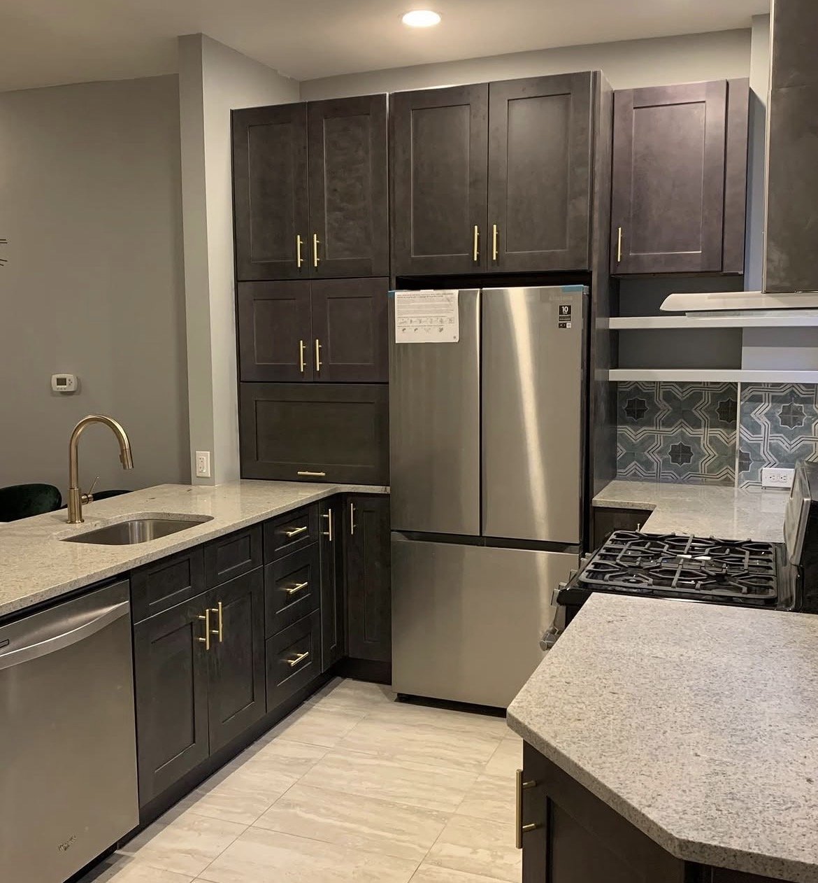 Modern kitchen with dark cabinets, stainless steel refrigerator, gas range, granite countertops, and a decorative backsplash with geometric patterns.