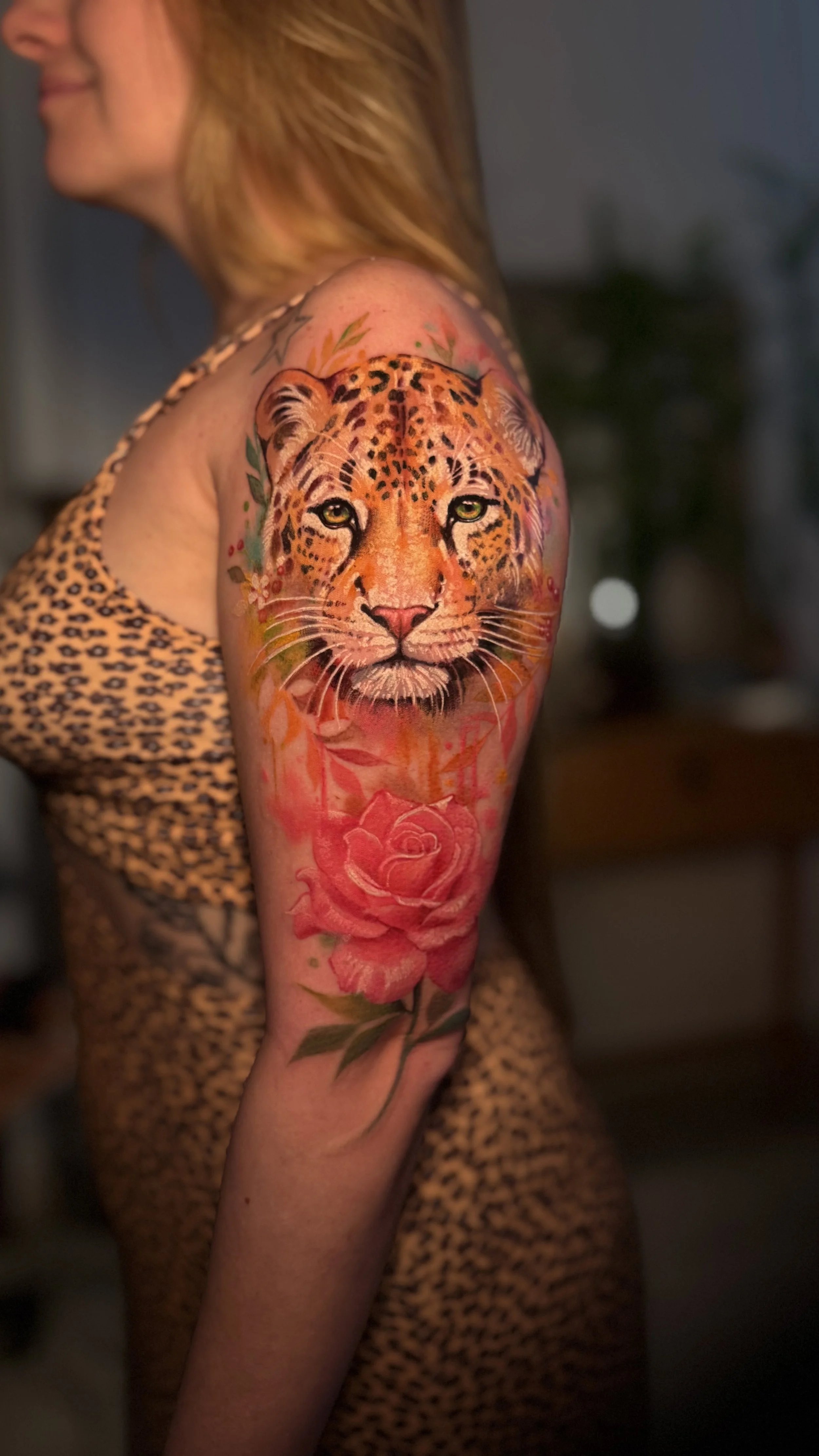 Tattoo of a realistic cheetah face on a woman's upper arm, with a large pink rose below it.