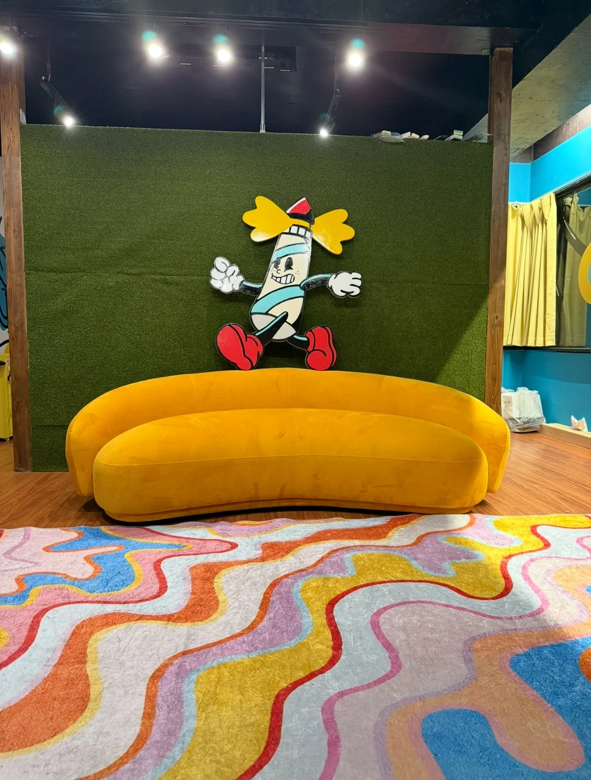 Colorful room with a vibrant wavy patterned carpet, a yellow velvet sofa, a green textured wall with a cartoon whale character, and yellow curtains.