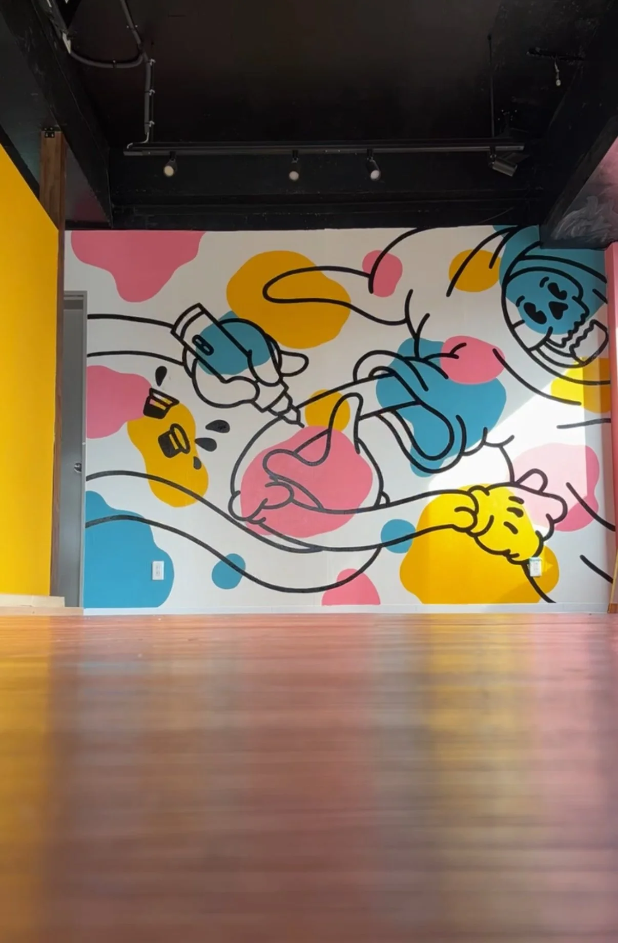 Colorful mural featuring a cartoon-like drawing of two young children playing with a water gun, with abstract pink, yellow, and blue shapes in the background.