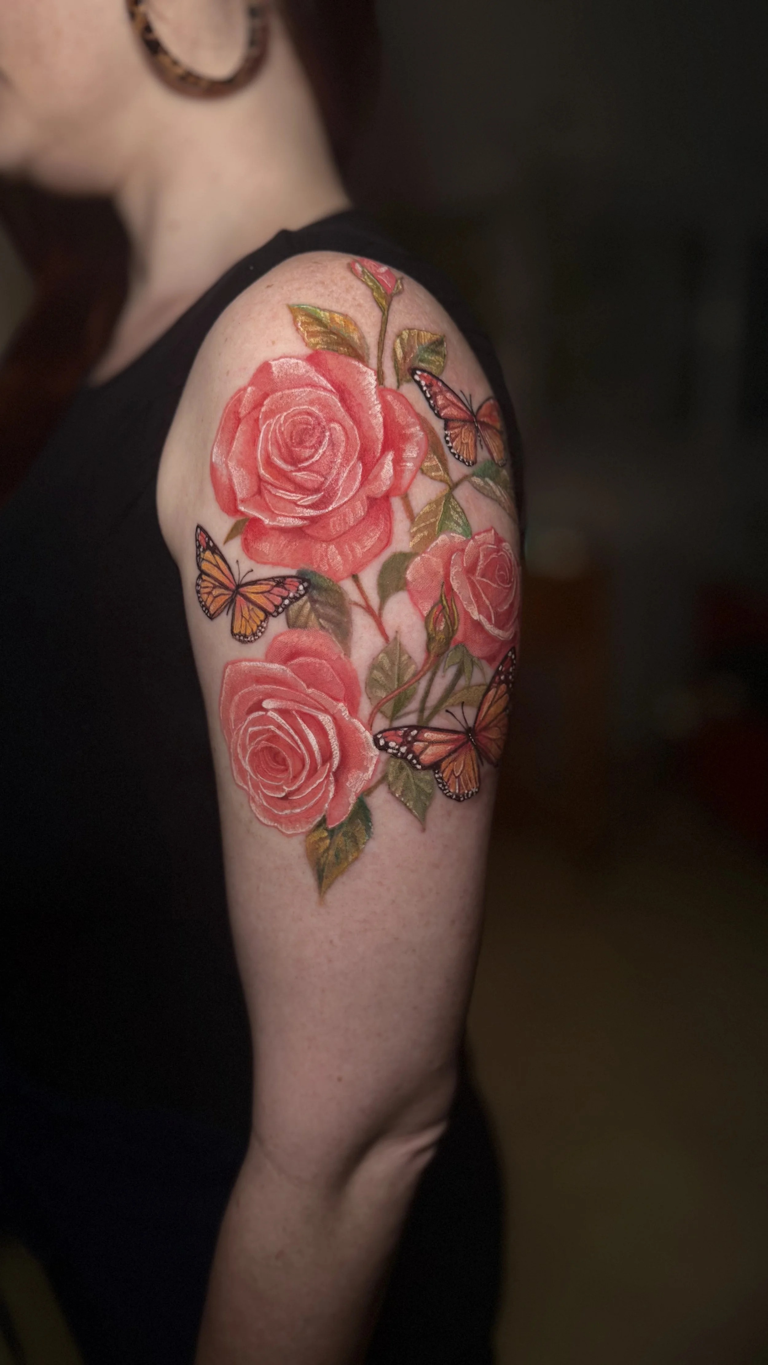 Tattoo of pink roses and orange flowers on upper arm.