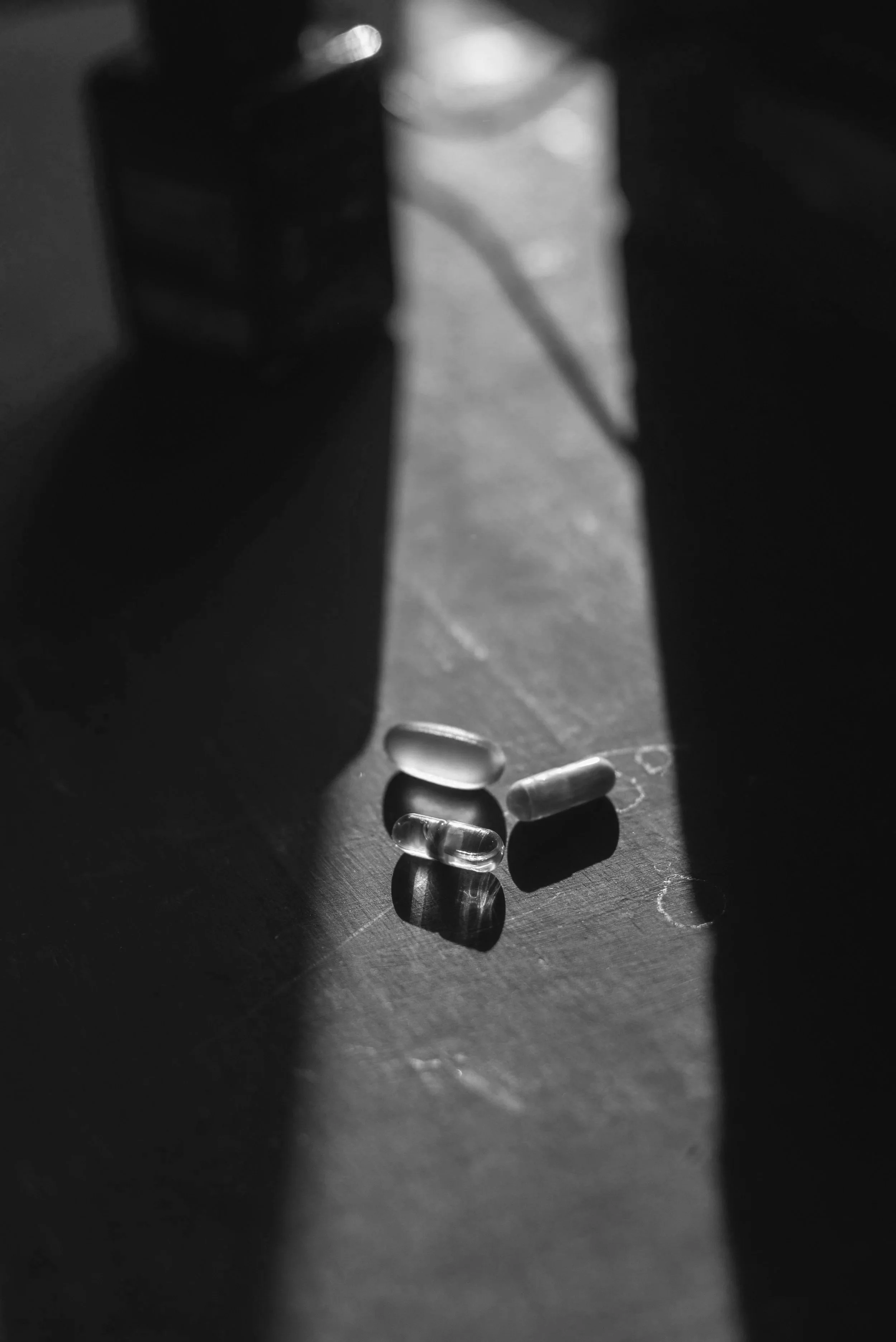 A few pills and capsules on a dark surface illuminated by a beam of light, with shadows cast around them.