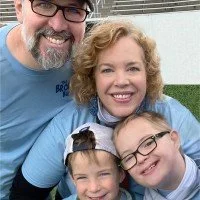A smiling family of four outdoors, with a man, woman, and two children, all close together.