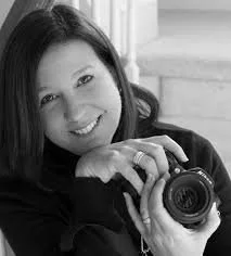 A woman taking a selfie with a camera, smiling and looking at the camera, in black-and-white.