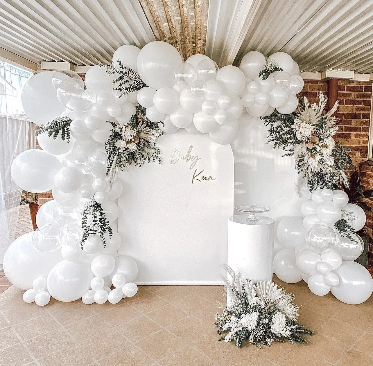 White balloon decorations with floral arrangements and a white backdrop with gold write that says "Baby Kear."