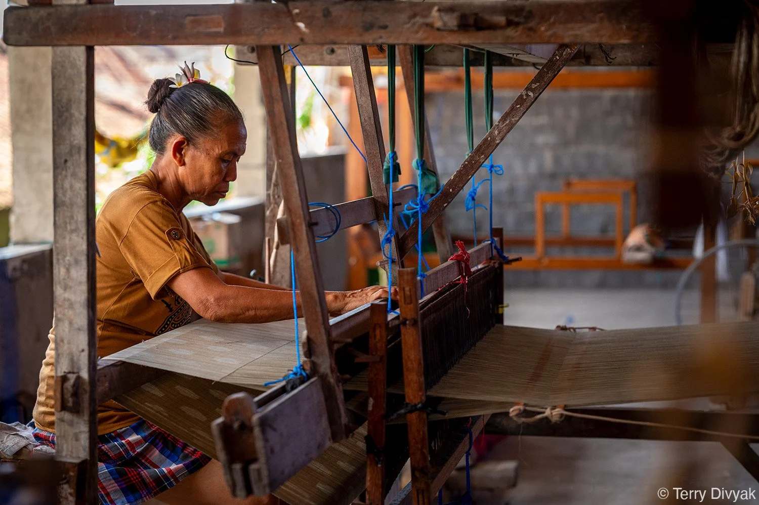 An older woman operating a traditional wooden loom, weaving fabric in a rustic workshop.