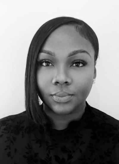 A woman with curly hair wearing glasses, earrings, and layered necklaces, smiling.