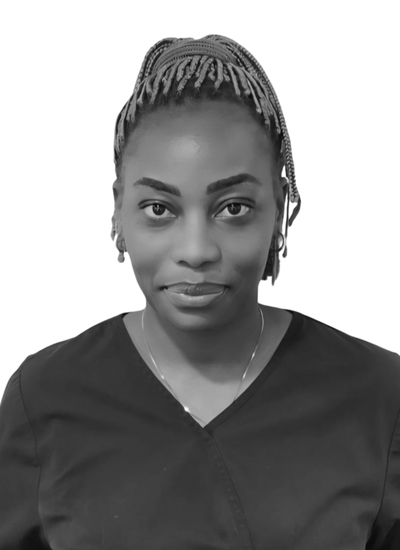 A young Asian woman with shoulder-length black hair, smiling in a blue top, standing outdoors with green foliage in the background.