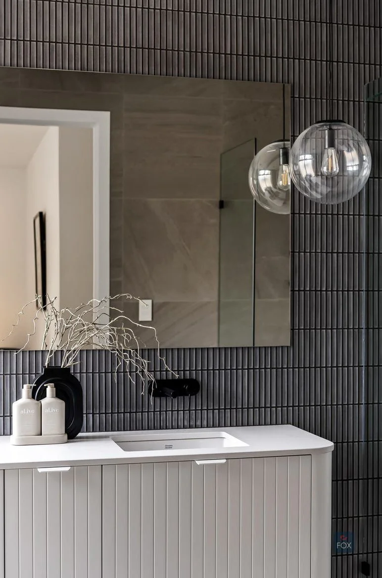 Modern bathroom vanity with a white cabinet, black wall-mounted faucet, large mirror, round glass light fixtures, and decorative items on the countertop.