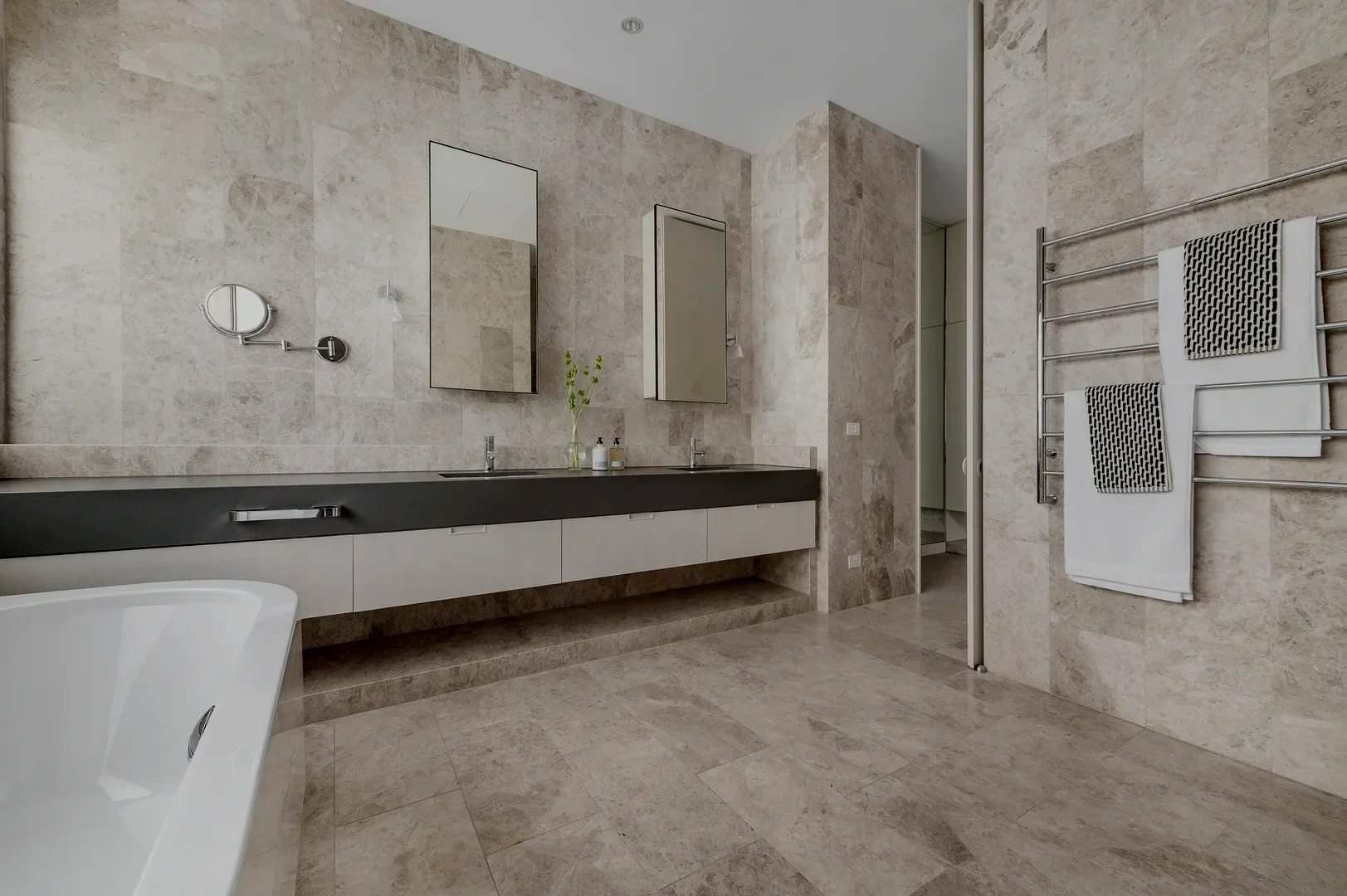 Modern shower with a rain shower head and a secondary handheld showerhead on a wall with gray tiles and a pink textured accent panel with LED lighting.