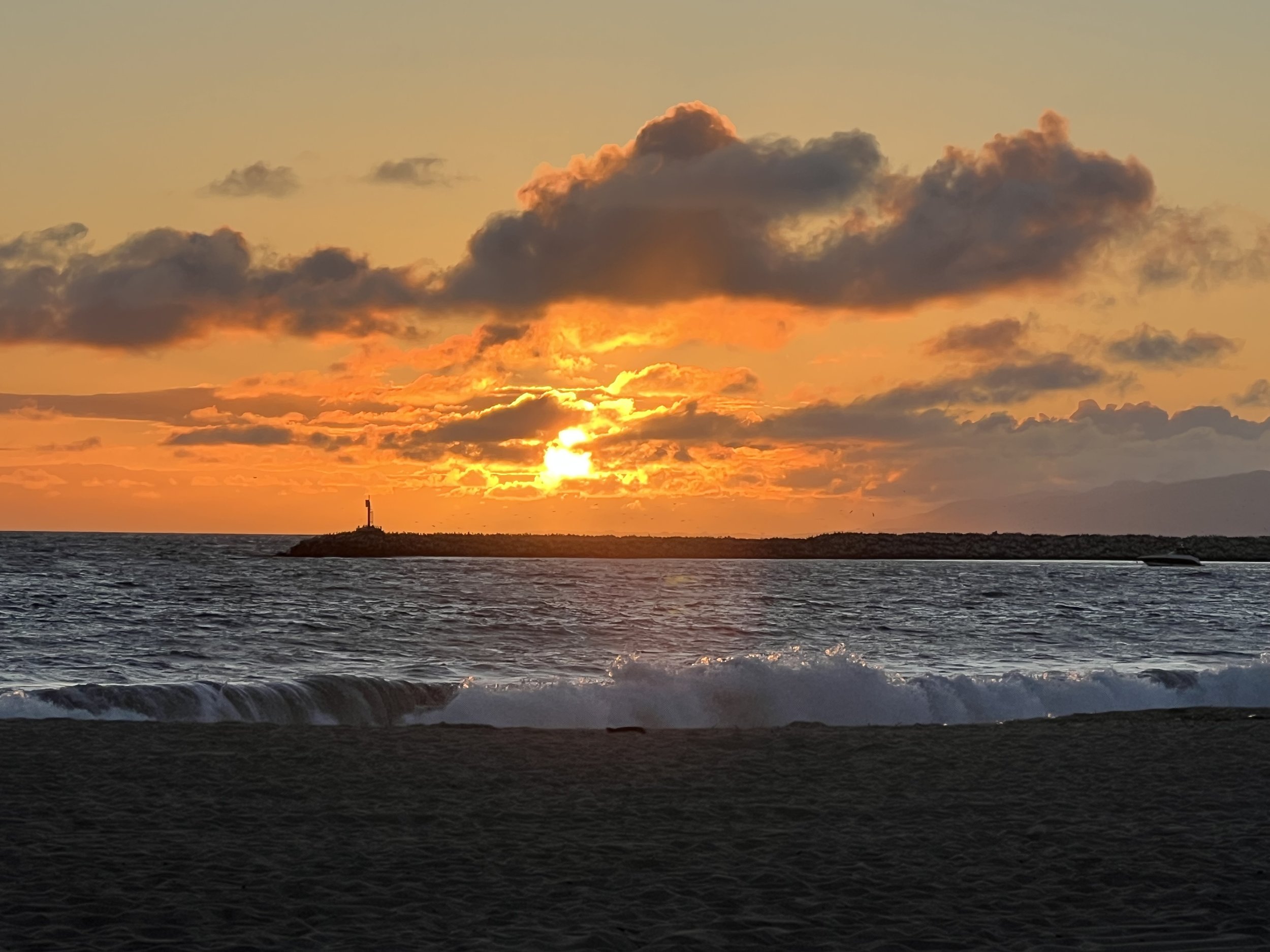 Sunset over the ocean with clouds in the sky and a lighthouse on a small island in the distance.