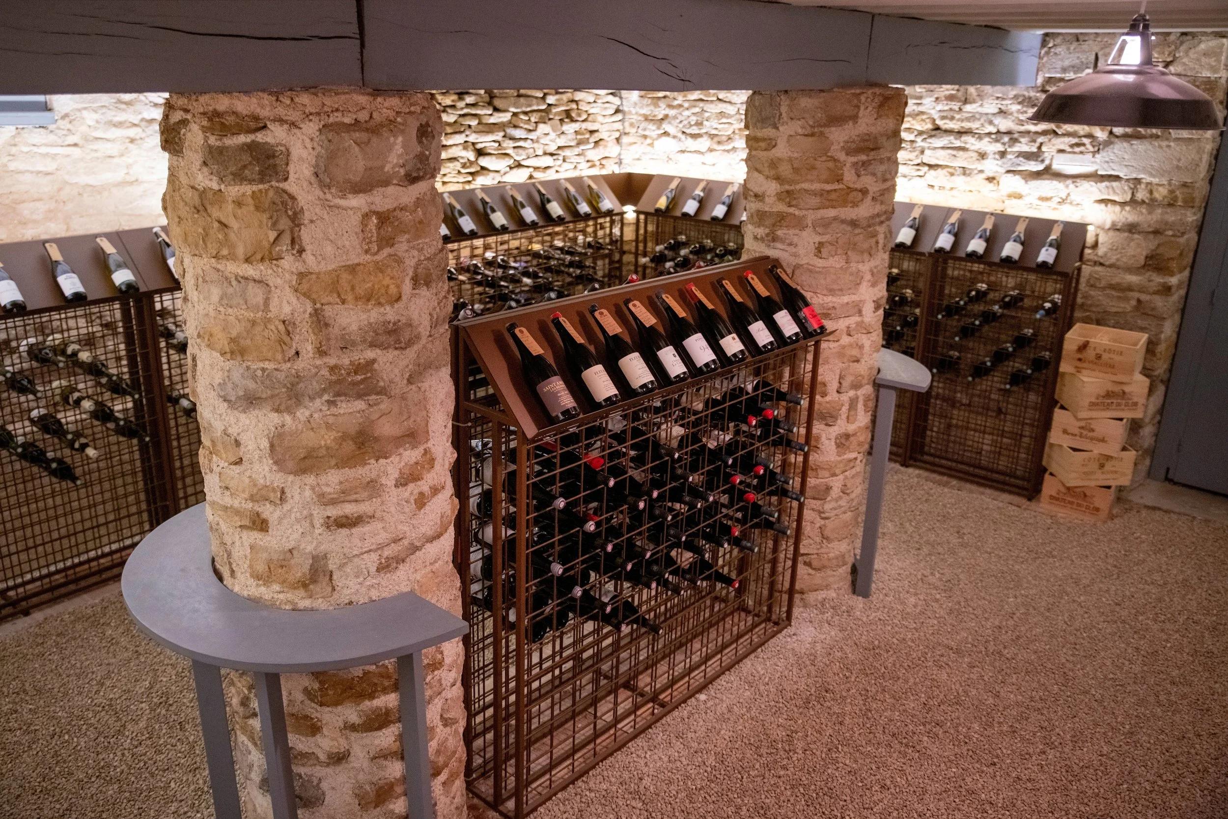 Wine bottles on wood racks and metal wine racks against a stone wall in an underground cellar.