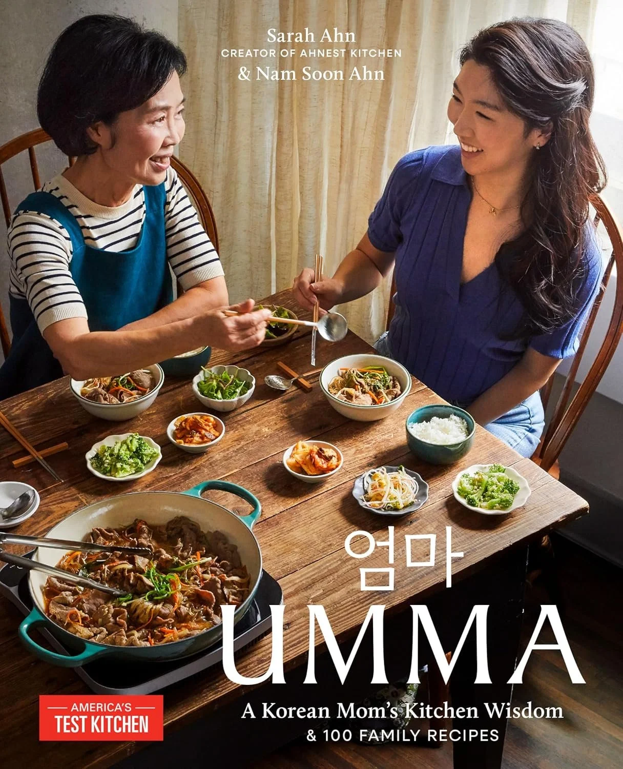 A Korean mother and daughter sitting at a wooden dining table with various Korean dishes, smiling and sharing a meal together.