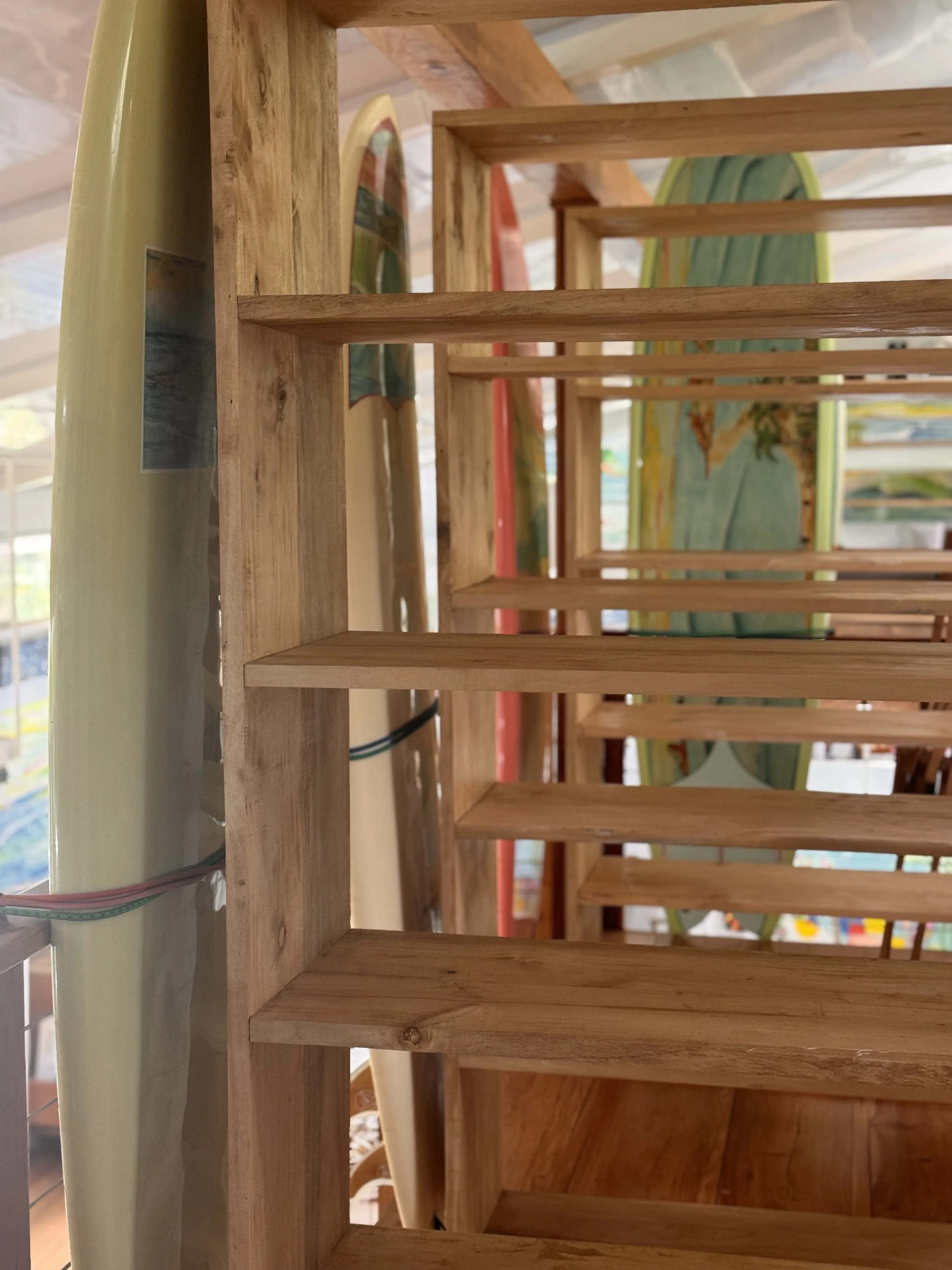 Close-up of wooden rack or shelf with evenly spaced horizontal slats, with surfboards in the background.